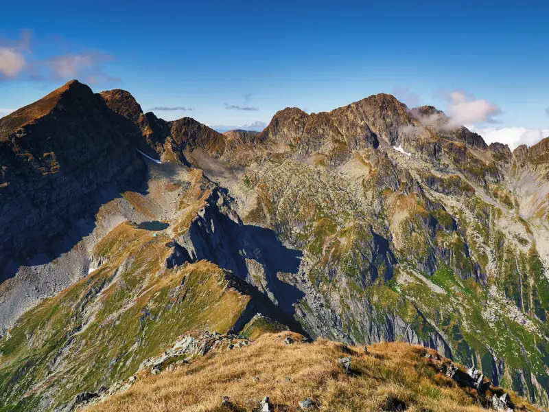 Blick von einem Grat auf die felsige Gipfelkette des Fagaras-Gebirges in den Karpaten mit einem kleinen Bergsee.