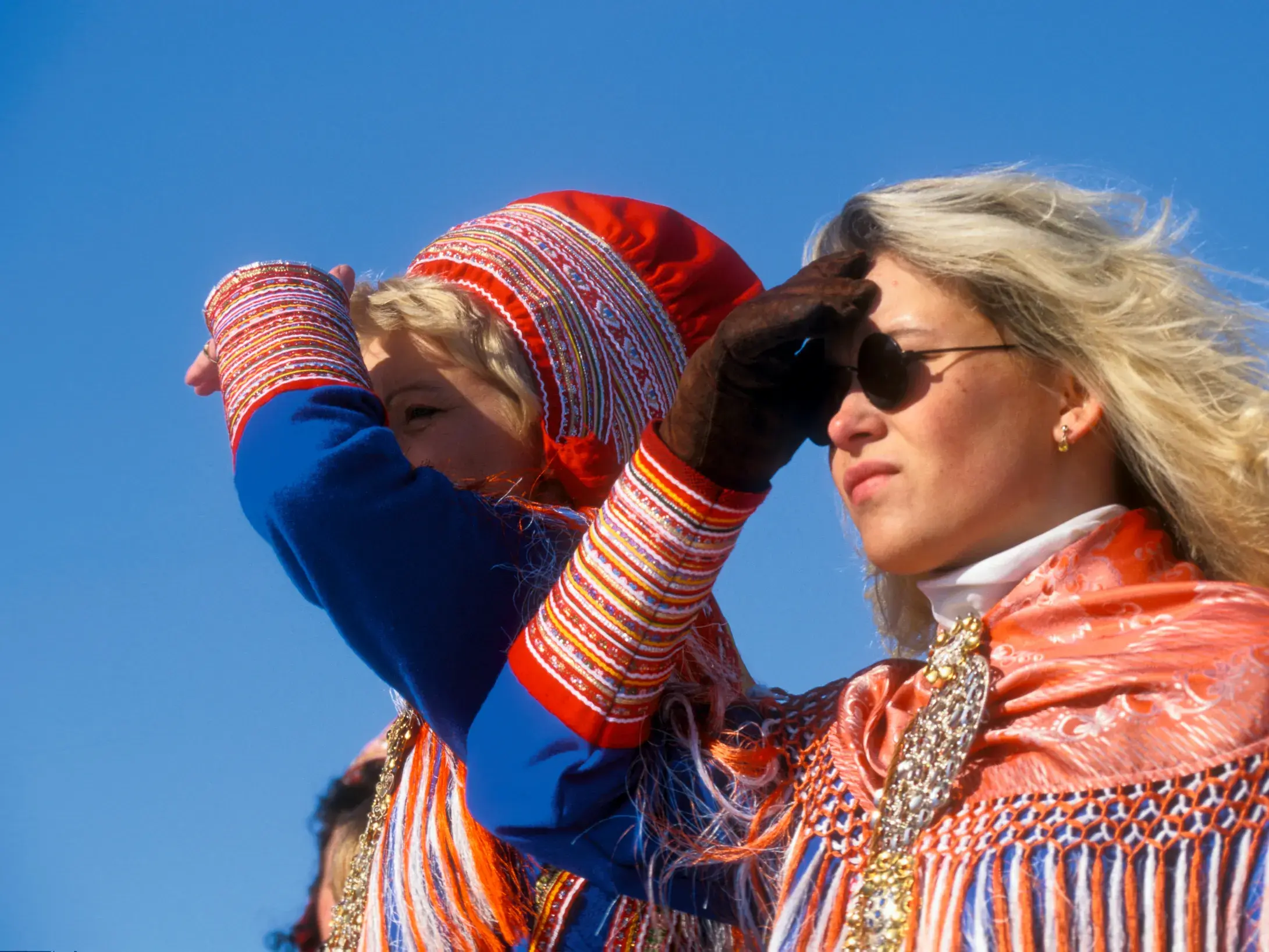 Eine junge Frau in der traditionellen Tracht der Sámi blickt mit einer Begleiterin in die sonnige Weite Lapplands.
