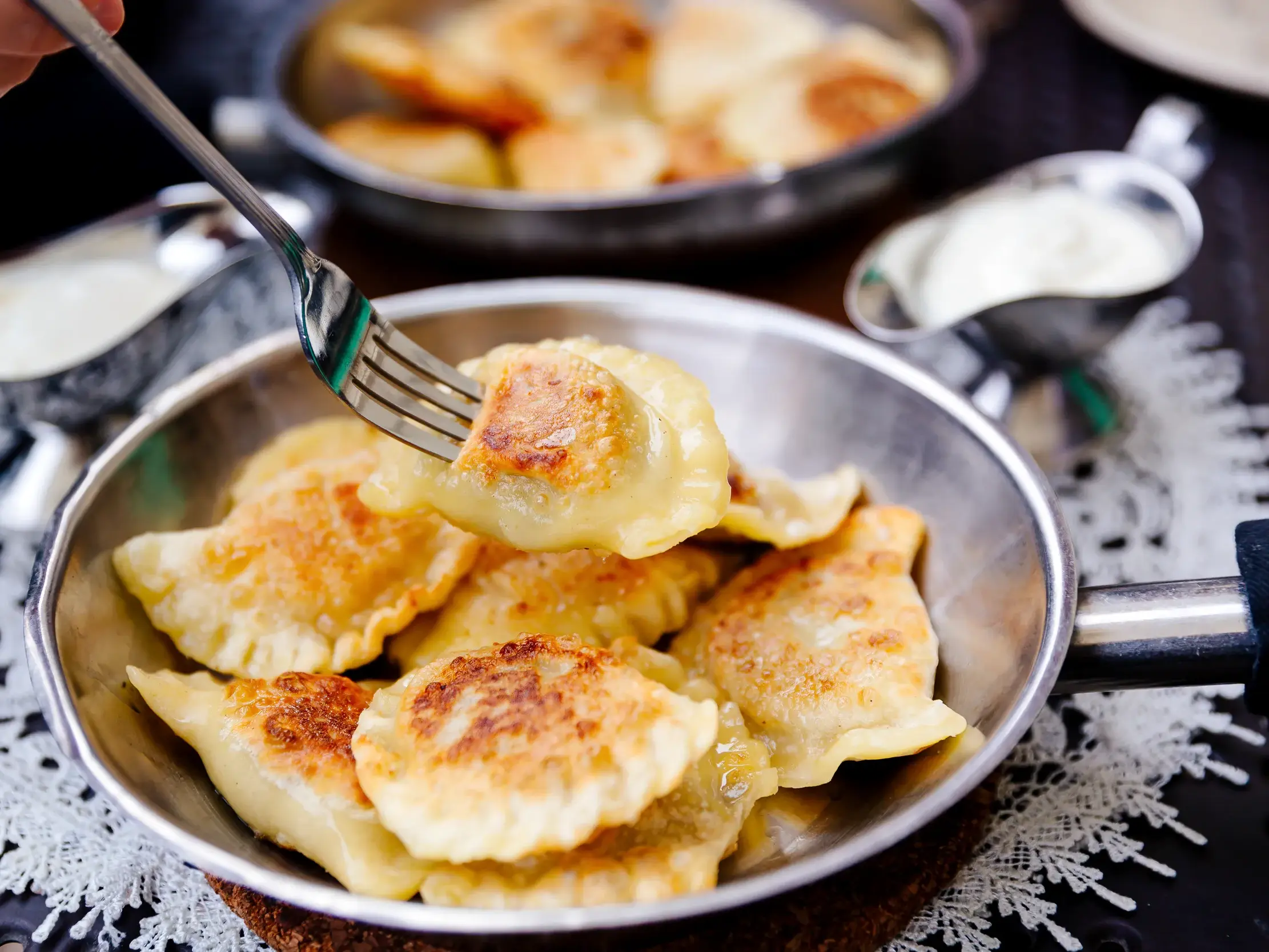 Eine Gabel hebt eine goldbraun gebratene Pierogi aus einer Metallpfanne. Typisches Gericht einer Reise durch Polen.