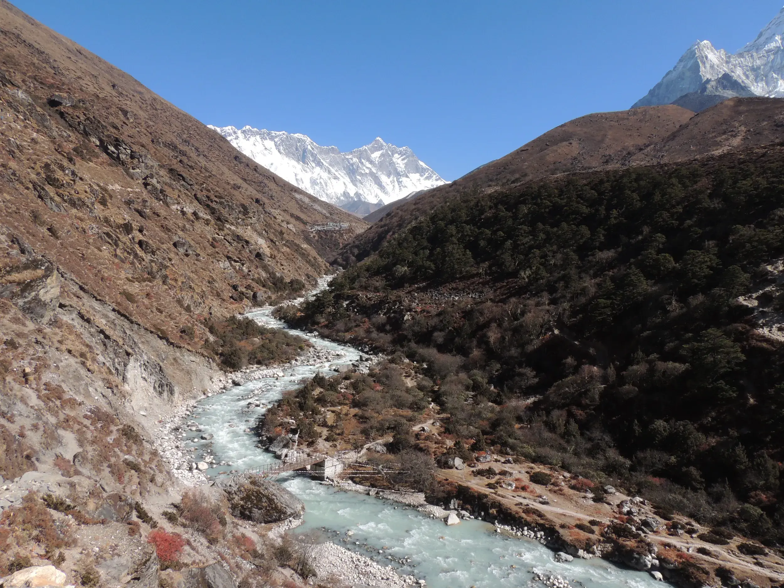 Der türkisfarbene Fluss Dudh Kosi auf dem Trekkingpfad durch das Khumbu-Tal mit schneebedeckten Himalaya-Gipfeln im Hintergrund.