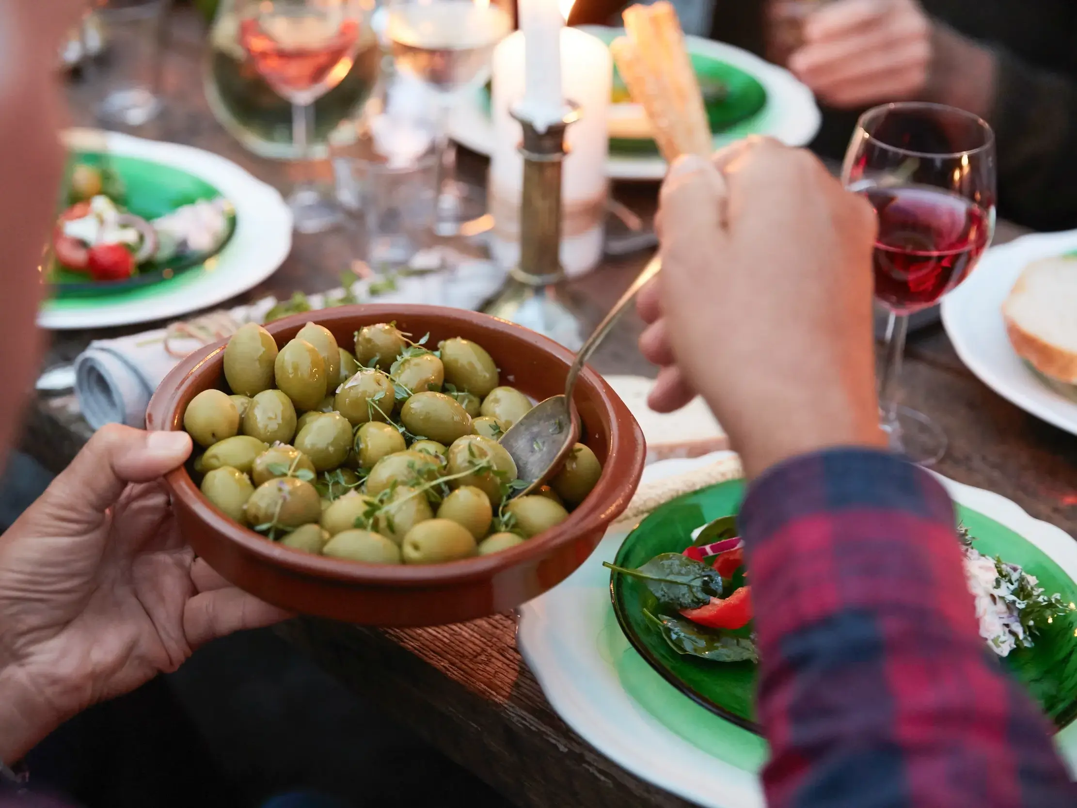 Eine Person reicht eine Tonschale mit grünen Oliven bei einem gemütlichen Abendessen mit kroatischen Spezialitäten und Wein.