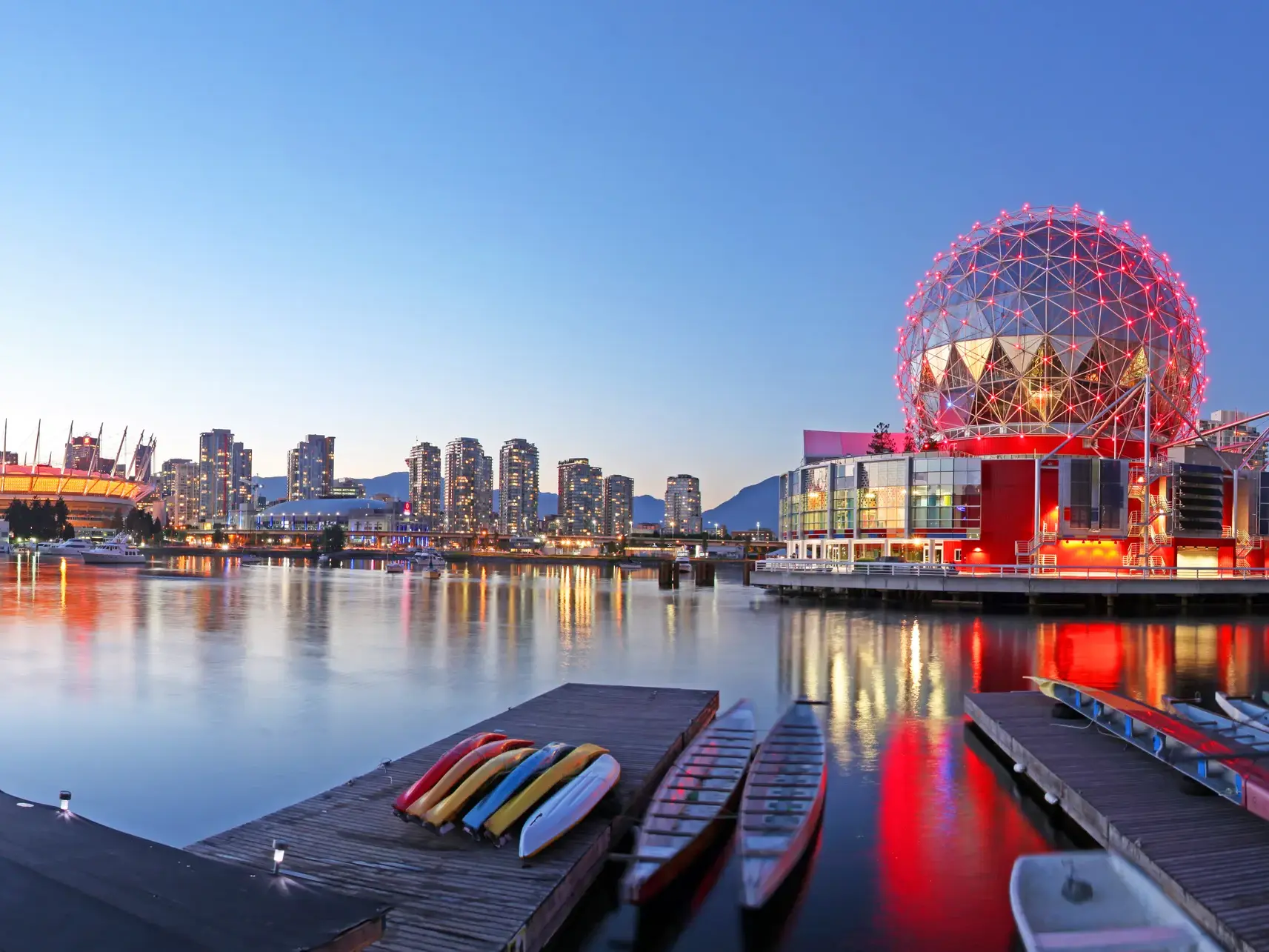 Das rot beleuchtete Science World und die Skyline von Vancouver spiegeln sich im False Creek bei Dämmerung.