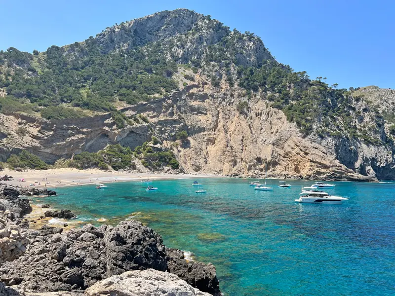Blick von einem Wanderweg in der Serra de Tramuntana auf eine idyllische Bucht mit Booten im türkisblauen Mittelmeer.