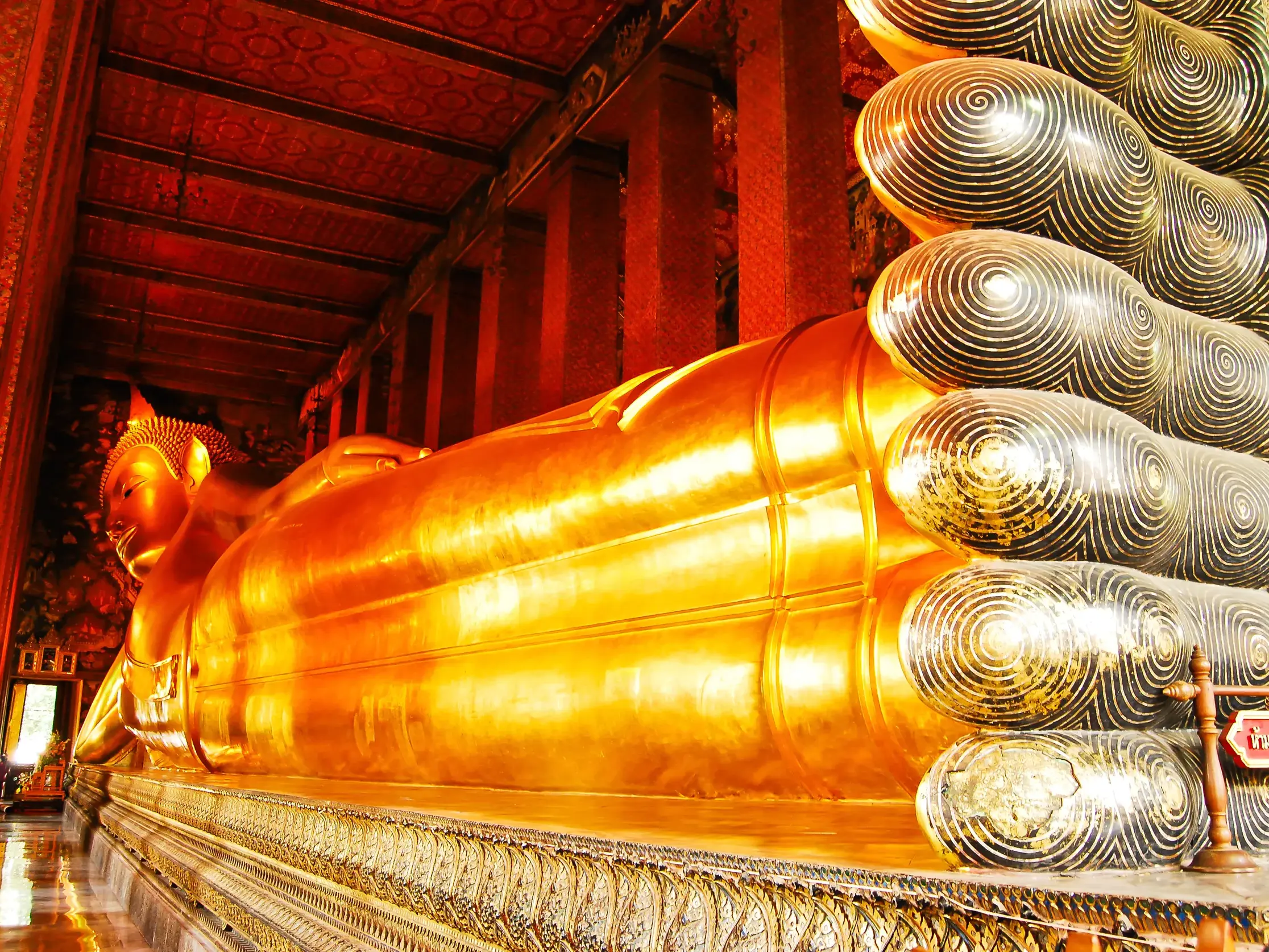 Die riesige, goldene Statue des liegenden Buddha im Wat Pho in Bangkok, mit Fokus auf die kunstvoll verzierten Fußsohlen.