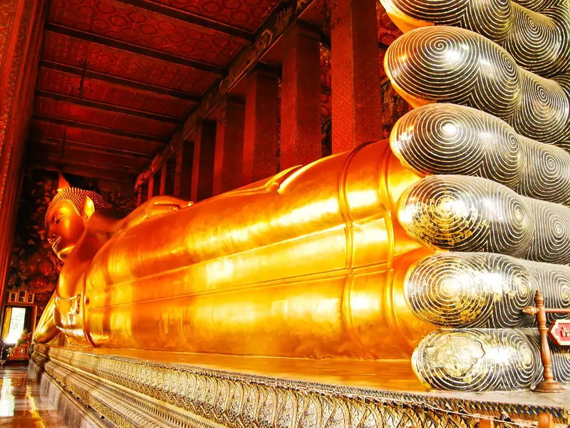Die riesige, goldene Statue des liegenden Buddha im Wat Pho in Bangkok, mit Fokus auf die kunstvoll verzierten Fußsohlen.