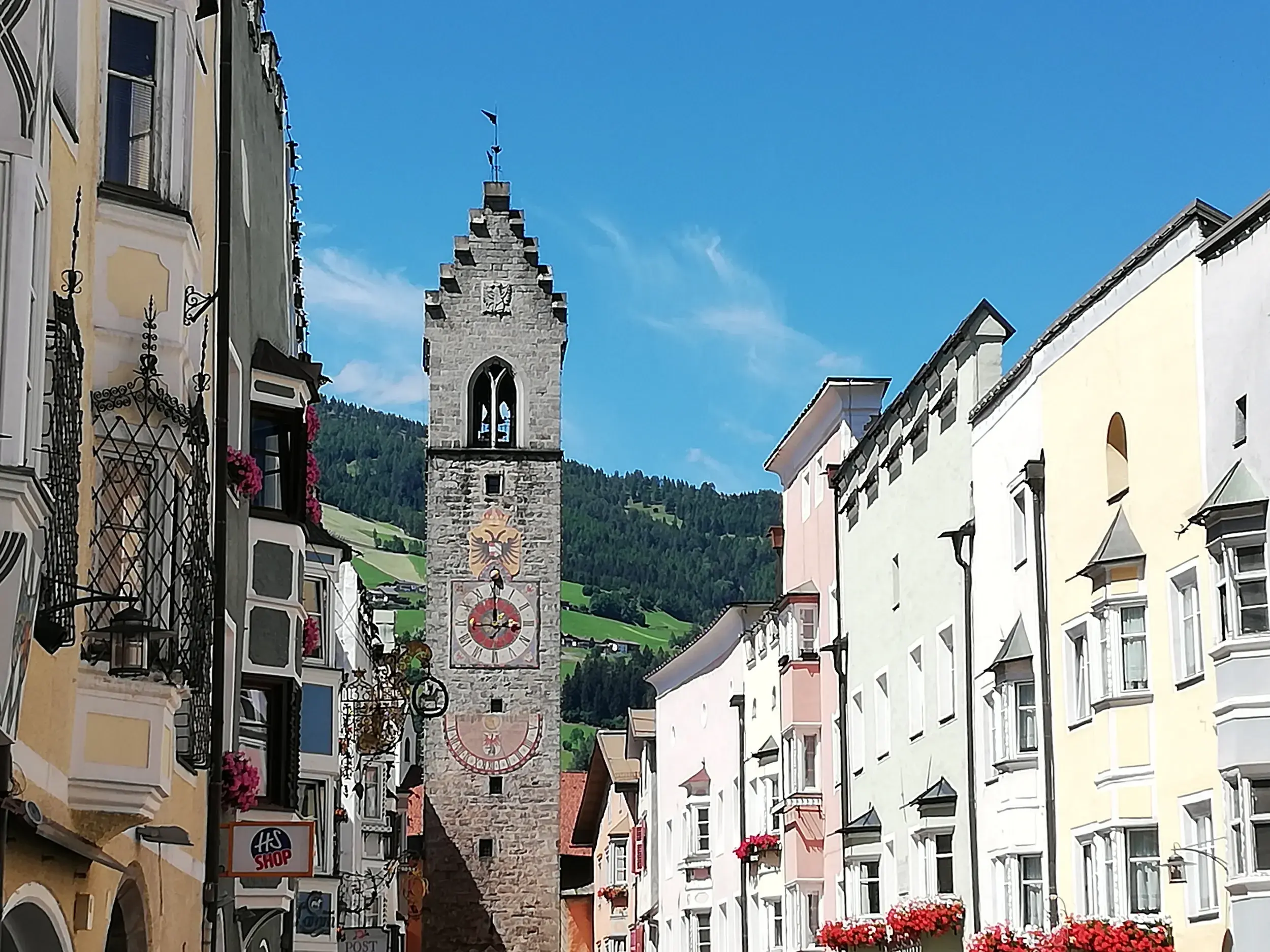 Historischer Zwölferturm in der Altstadt von Sterzing umgeben von bunten Häusern und der Bergkulisse Südtirols.
