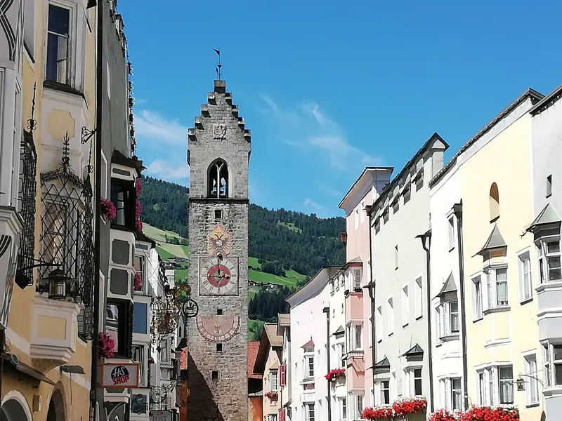 Historischer Zwölferturm in der Altstadt von Sterzing umgeben von bunten Häusern und der Bergkulisse Südtirols.