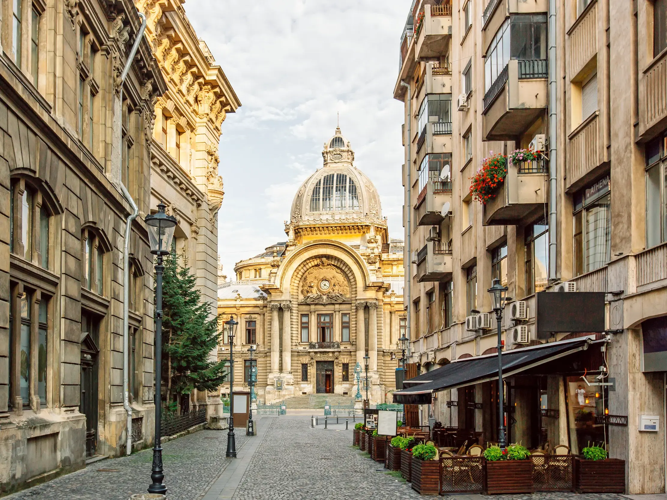 Malerische Gasse in der Altstadt von Bukarest mit historischen Gebäuden und Blick auf einen imposanten Bau mit einer großen Glaskuppel.