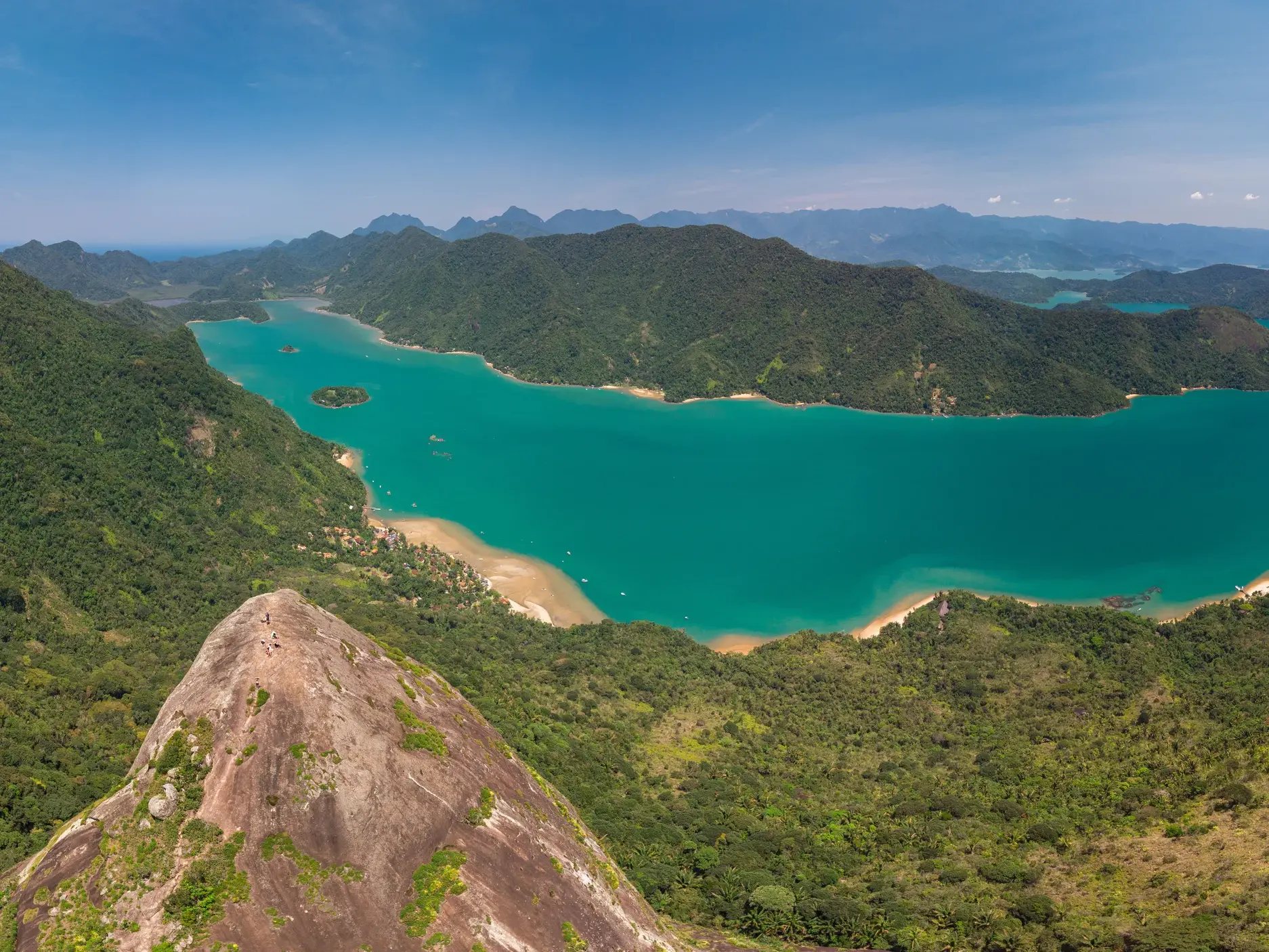 Zwei Wanderer auf dem felsigen Gipfel des Mamanguá Peak genießen den Panoramablick auf die türkise Bucht von Mamanguá.