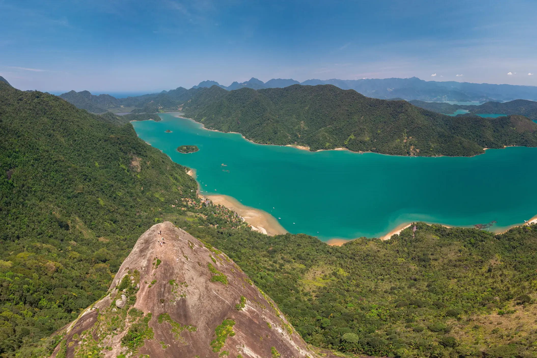 Zwei Wanderer auf dem felsigen Gipfel des Mamanguá Peak genießen den Panoramablick auf die türkise Bucht von Mamanguá.
