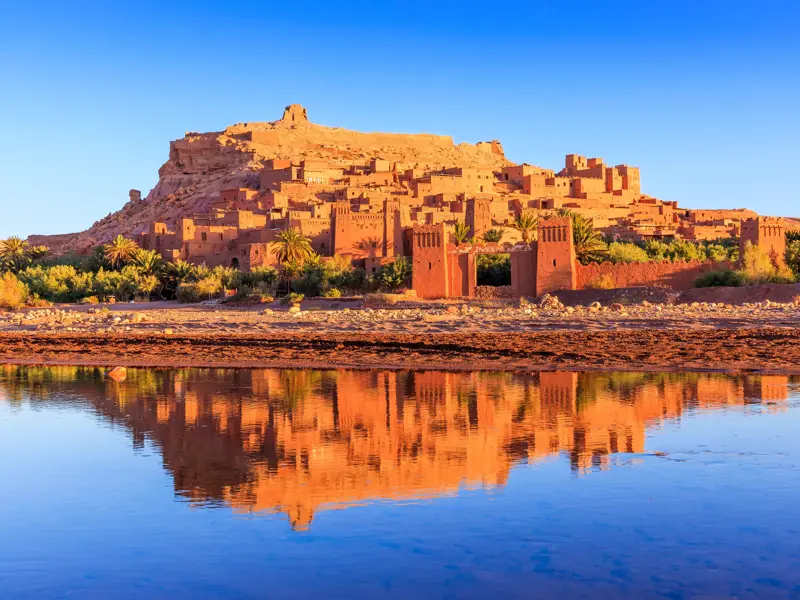 Die berühmte Berberburg Ait Benhaddou in Marokko spiegelt sich im Morgenlicht perfekt im ruhigen Wasser des Ounila Flusses.