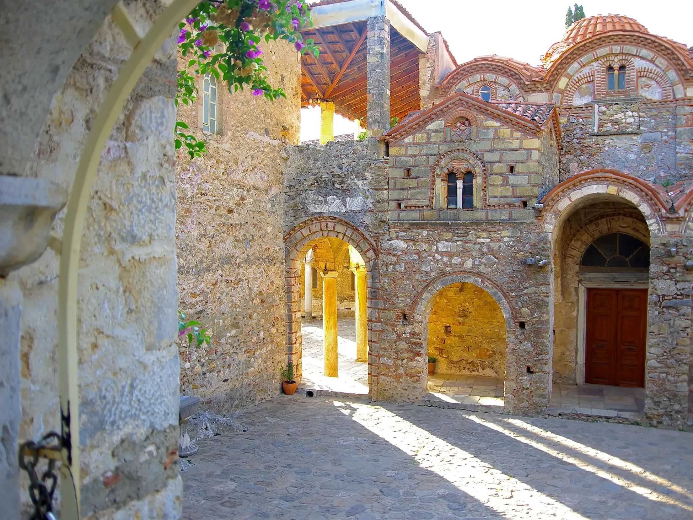 Sonniger Innenhof des Klosters Pantanassa in der byzantinischen Ruinenstadt Mistra mit Steinbögen und Kuppeldach.
