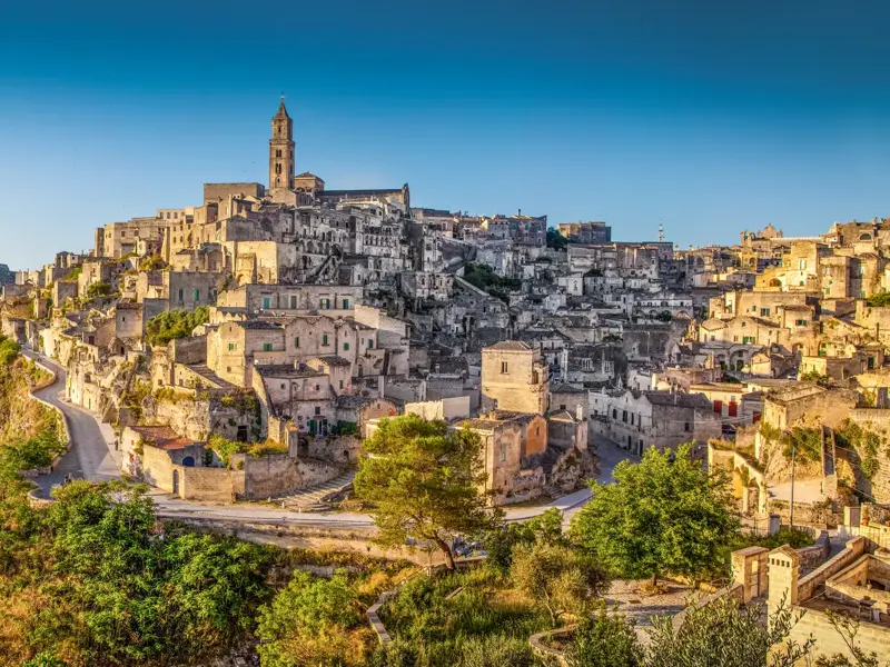 Panoramablick auf die historischen Sassi in Matera, UNESCO-Welterbe, mit ihren Steinhäusern und einem Kirchturm unter blauem Himmel.
