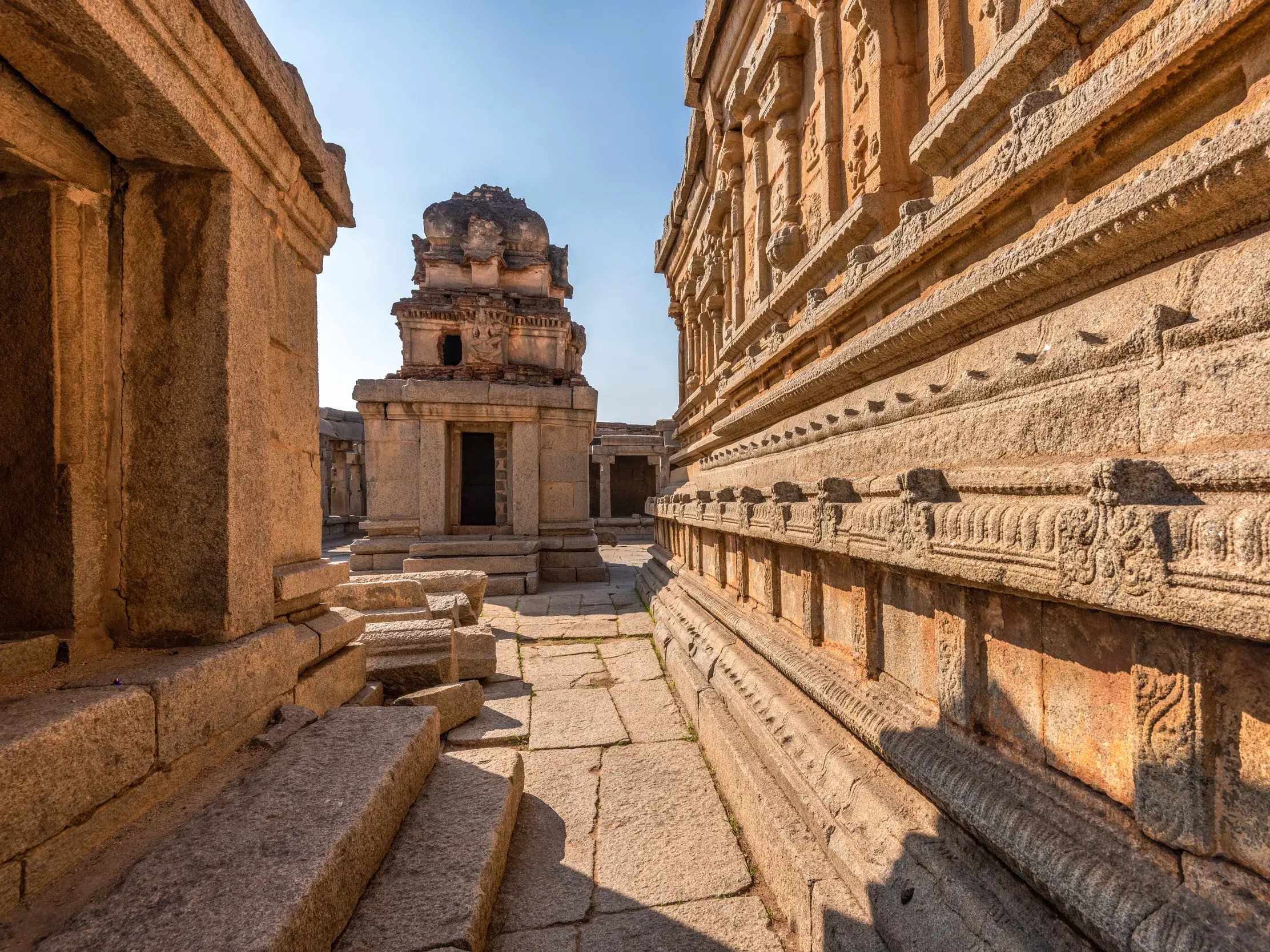 Sonniger Pfad durch die Tempelruinen von Vijayanagara in Hampi, einem UNESCO-Welterbe in Südindien.