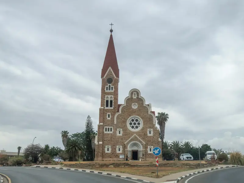 Die historische Christuskirche in Windhoek, Namibia, mit ihrer Steinfassade und dem roten Turmdach inmitten eines Kreisverkehrs.