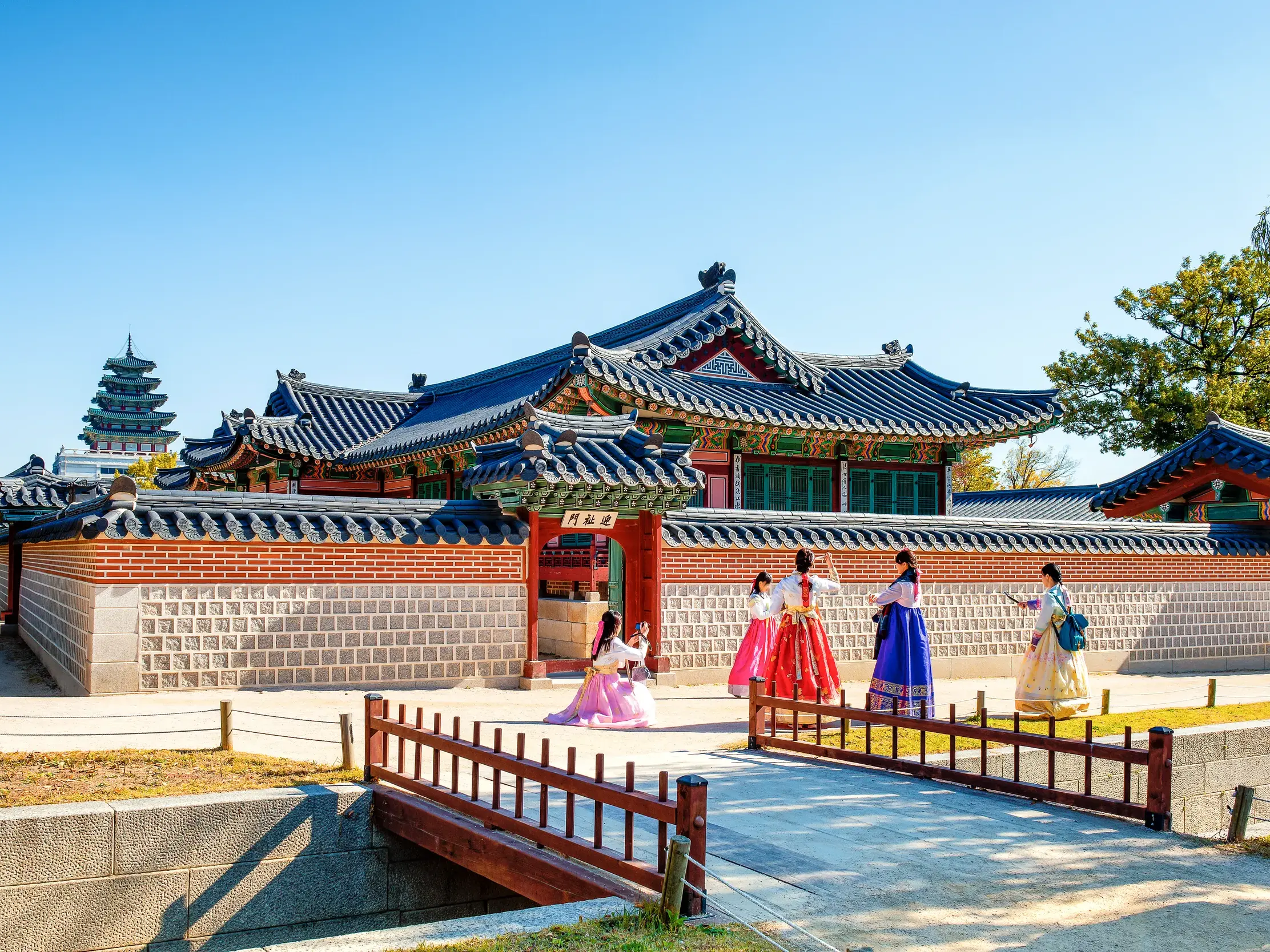 Vier Frauen in farbenfrohen Hanboks vor der traditionellen Architektur des Gyeongbok-Palastes in Seoul an einem sonnigen Tag.