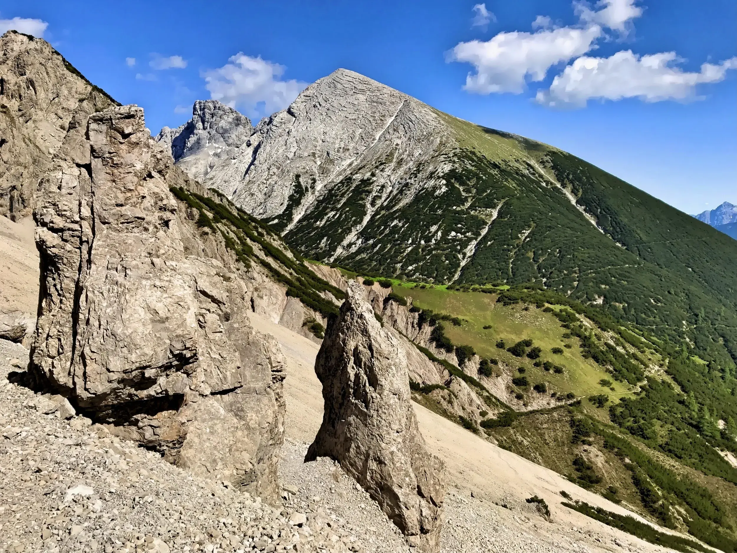 Markante Felsnadeln auf einem Geröllfeld vor der grünen Flanke des Großen Solsteins in der Erlspitzgruppe, Karwendel.