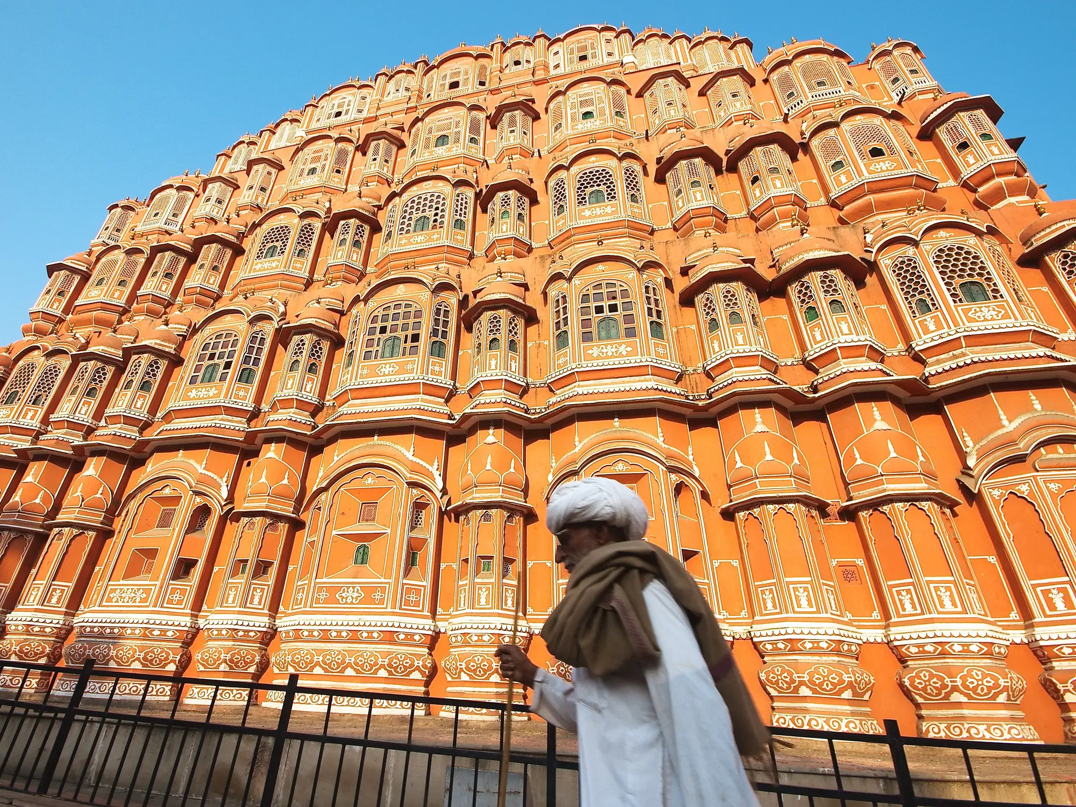 Einheimischer in traditioneller Kleidung vor der kunstvollen Fassade des Palastes der Winde, Hawa Mahal, in Jaipur.
