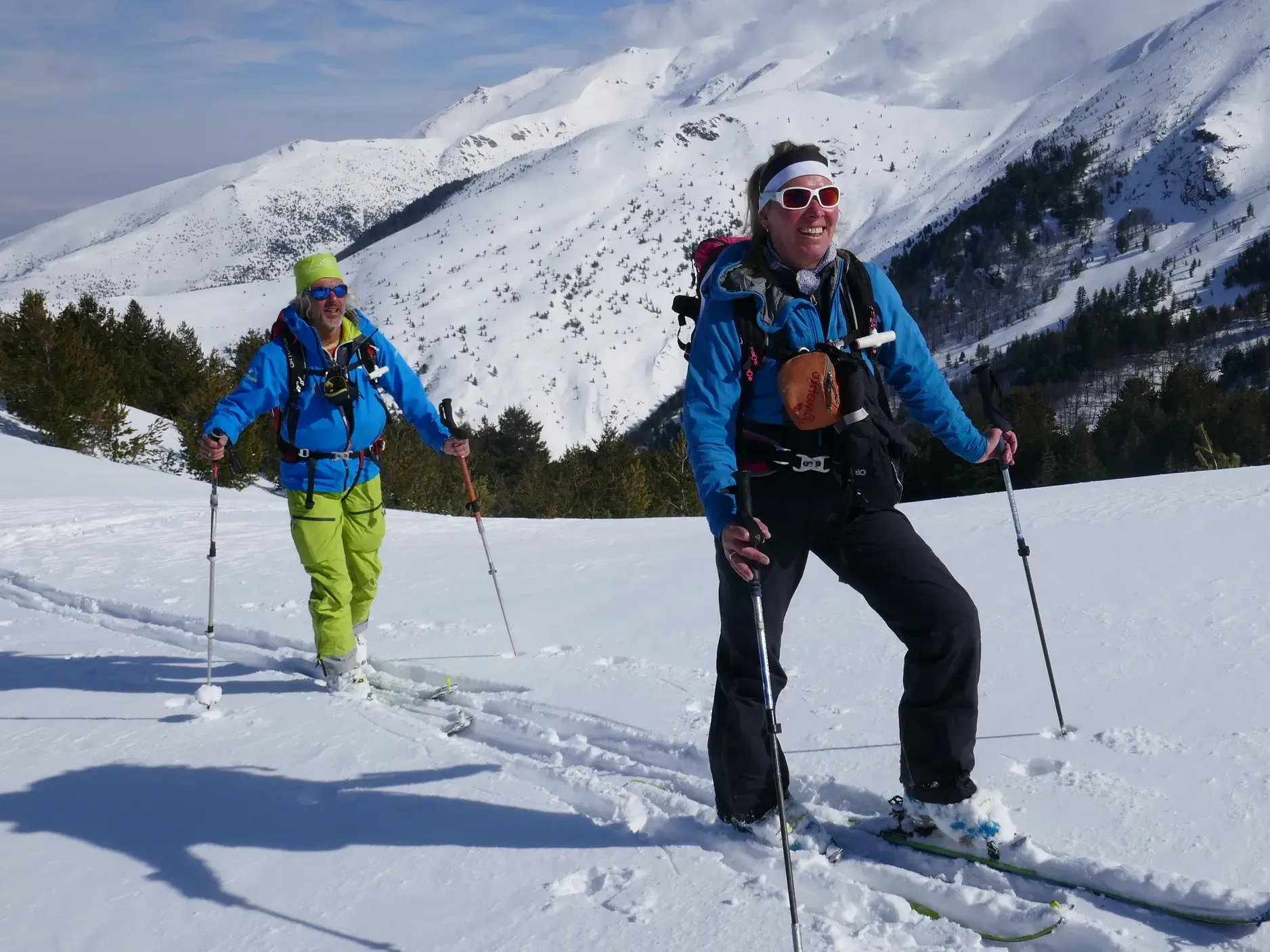 Zwei lachende Skitourengeher bei einer Tour im Pulverschnee vor der weiten Bergkulisse des Sharr-Gebirges im Kosovo.