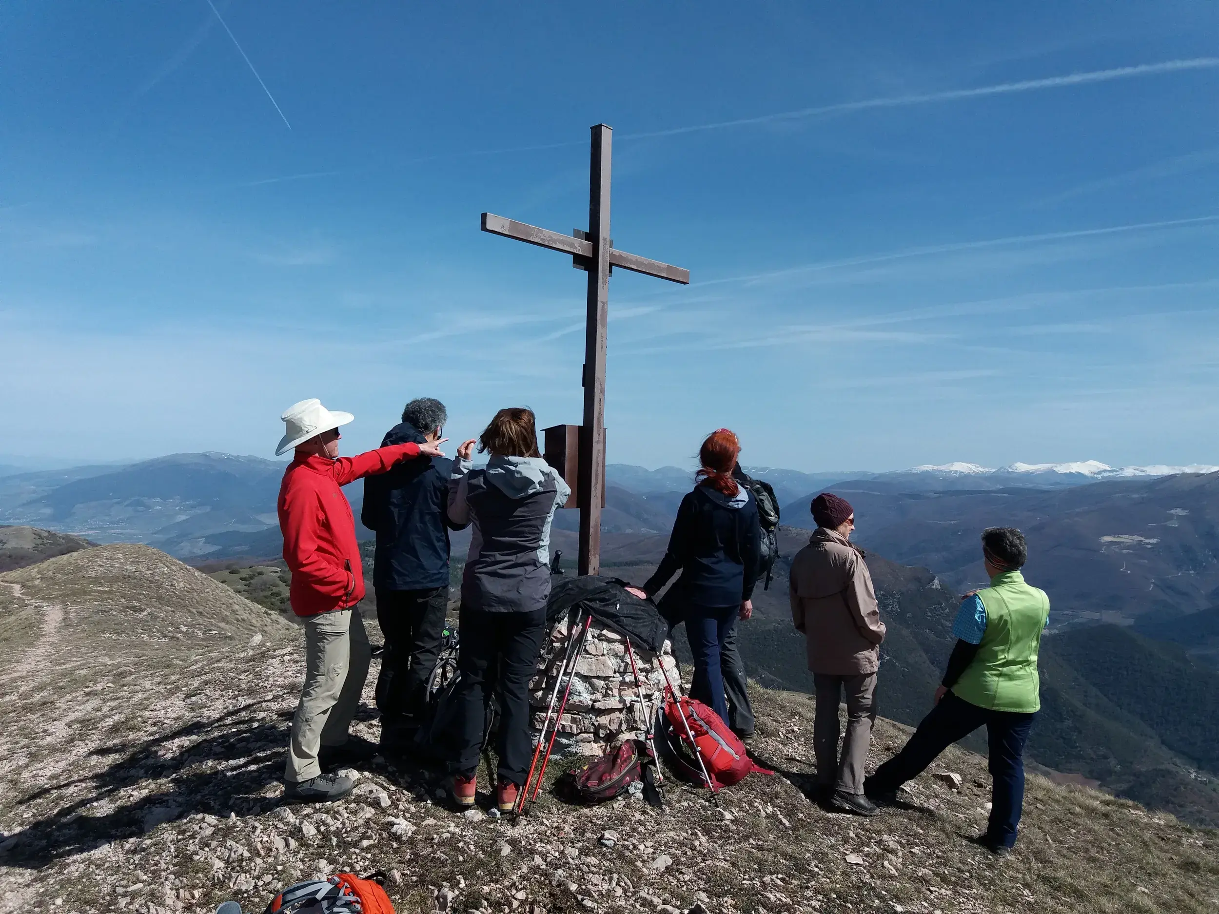 Hauser-Reisegruppe erreicht das Gipfelkreuz auf einer Wanderung und blickt auf die weite Bergkette der Sabiner Berge.