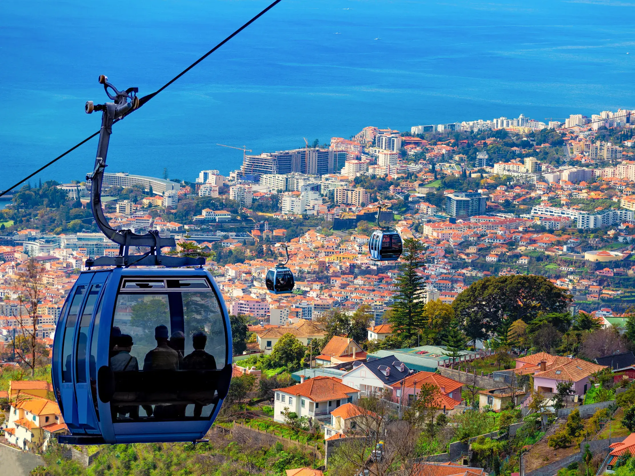 Eine Seilbahngondel mit Reisenden bietet einen Panoramablick über die Dächer der Hauptstadt Funchal bis zum Atlantik auf Madeira.