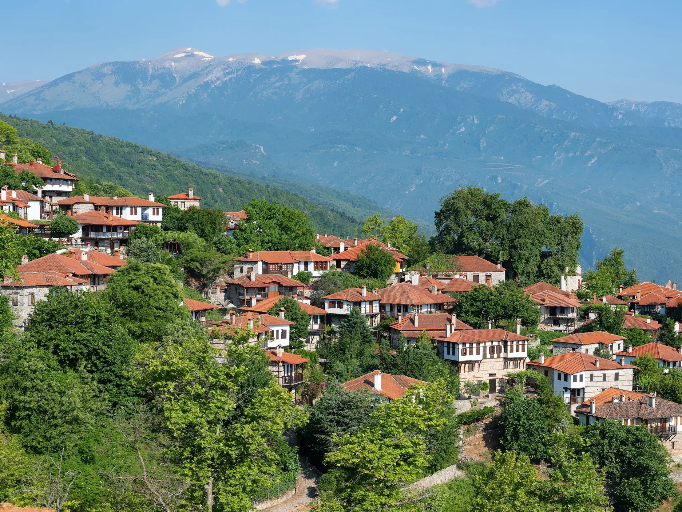 Das traditionelle Bergdorf Palaios Panteleimonas an einem grünen Hang, im Hintergrund das hohe Olymp-Massiv.
