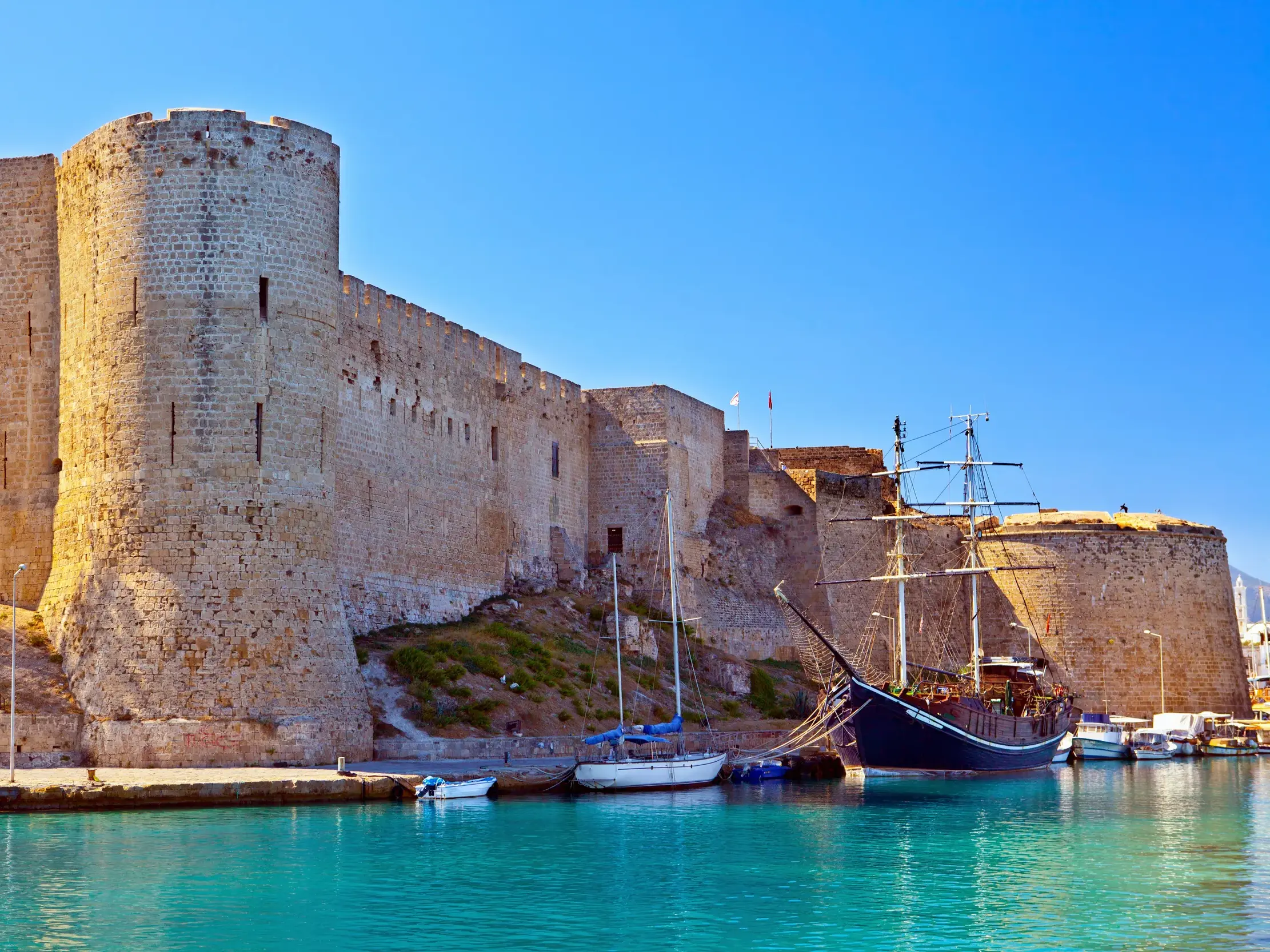 Die historische Hafenburg von Kyrenia ragt bei strahlendem Sonnenschein über den alten Hafen mit seinen Segelbooten.