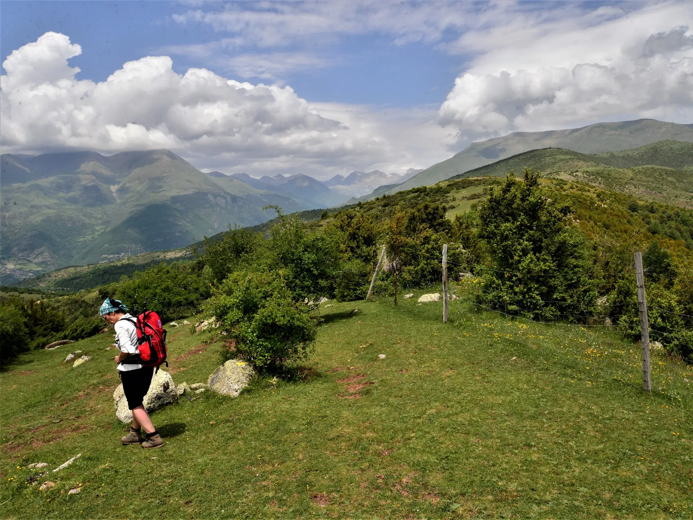 Eine Wanderin mit rotem Rucksack beim Trekking auf einem Wiesenpfad in den südlichen Pyrenäen mit Blick auf die Bergkette.