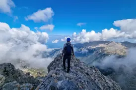 Ein Trekker genießt nach der Gipfelbesteigung die Aussicht vom felsigen Grat des Olymp-Massivs über die Wolken.