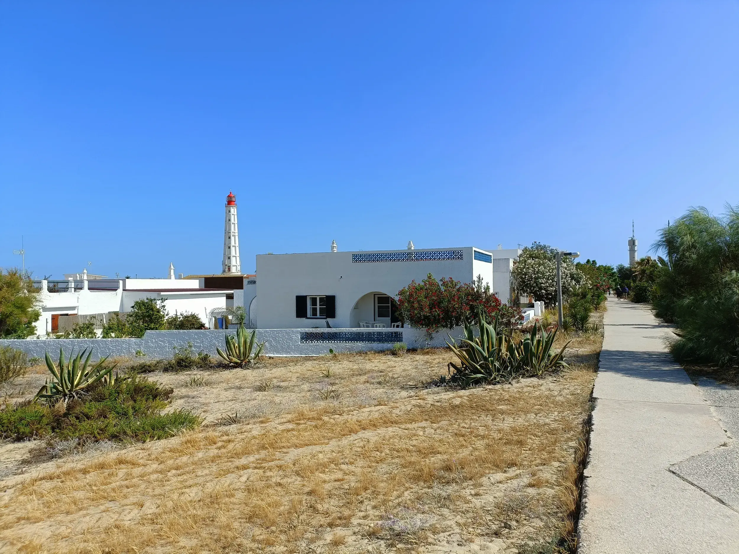 Küstenpfad auf der Insel Culatra führt vorbei an weißen Häusern zum Leuchtturm von Farol in der Algarve.