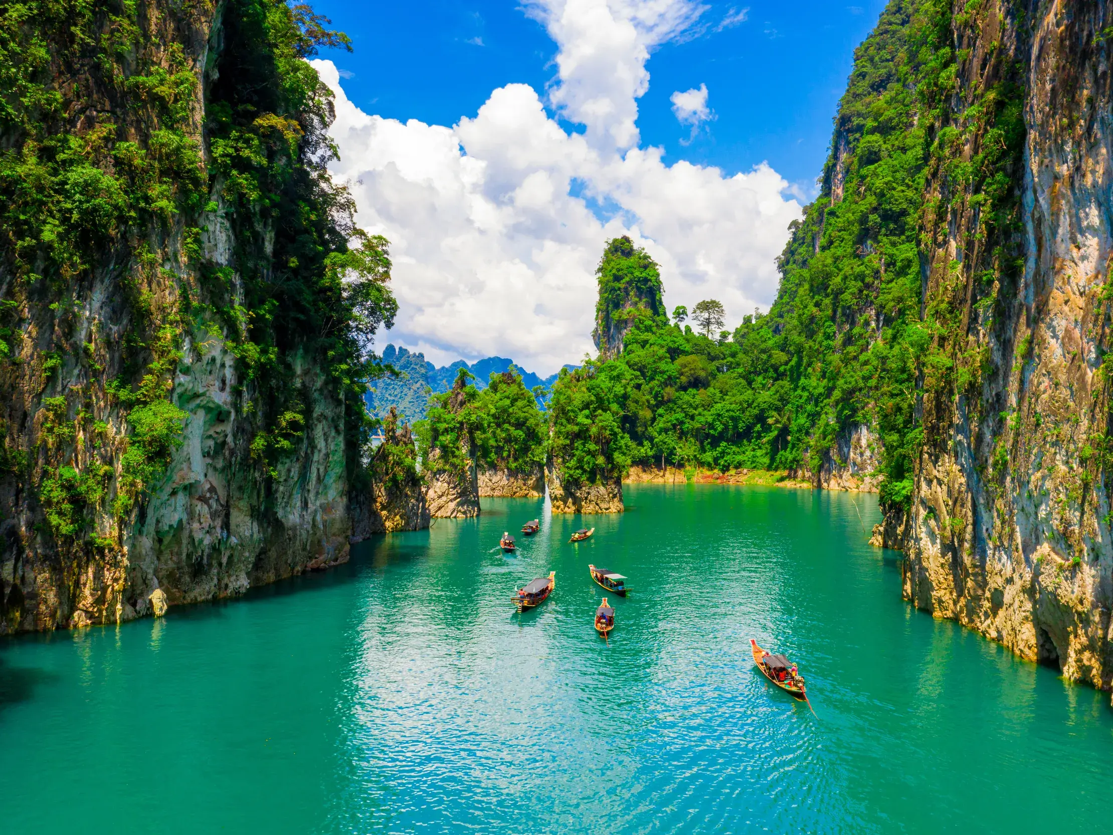 Eine Kleingruppe erkundet in Langschwanzbooten den türkisen Chiao-Lan-See im Khao-Sok-Nationalpark zwischen steilen Felsen.