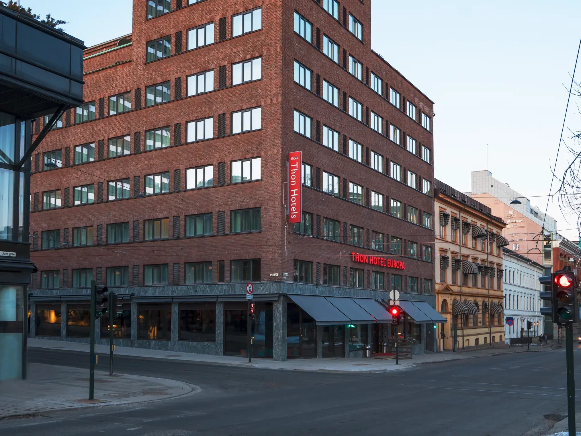 Modernes Backsteingebäude des Thon Hotel Europa an einer urbanen Straßenkreuzung im Zentrum von Oslo bei Dämmerung.