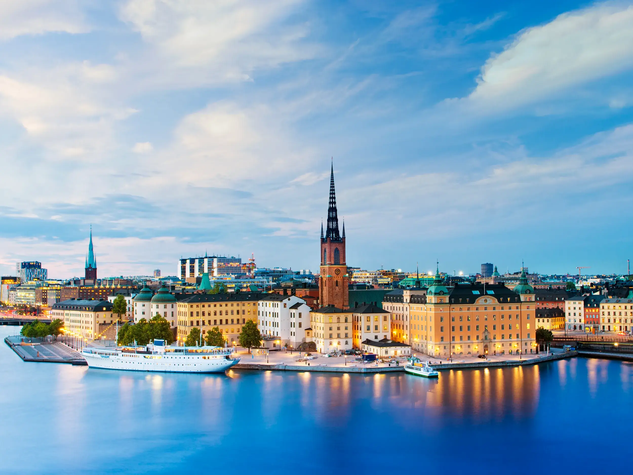 Die historische Altstadt Gamla Stan in Stockholm bei Dämmerung, mit der Riddarholmskyrkan und Spiegelungen im Wasser.