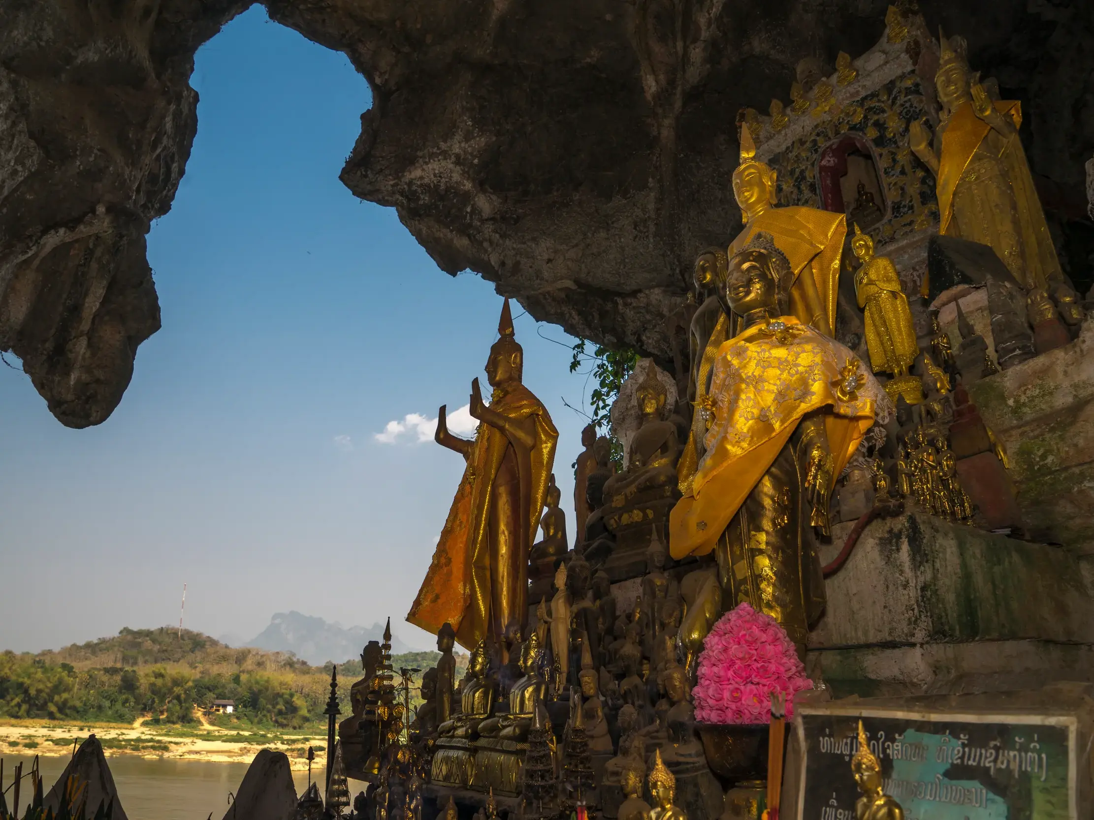 Heilige Pak Ou Höhlen in Laos: Goldene Buddha-Statuen mit Blick aus der Felsöffnung auf den Fluss Mekong und die Berge.