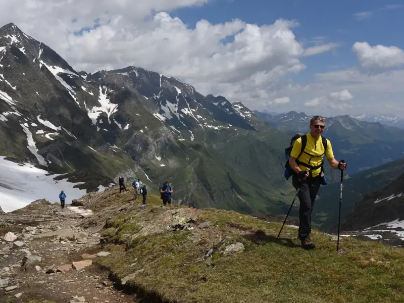 Eine Wandergruppe beim Trekking auf einem schmalen Grat des Meraner Höhenwegs mit Blick auf die Texelgruppe in Südtirol.