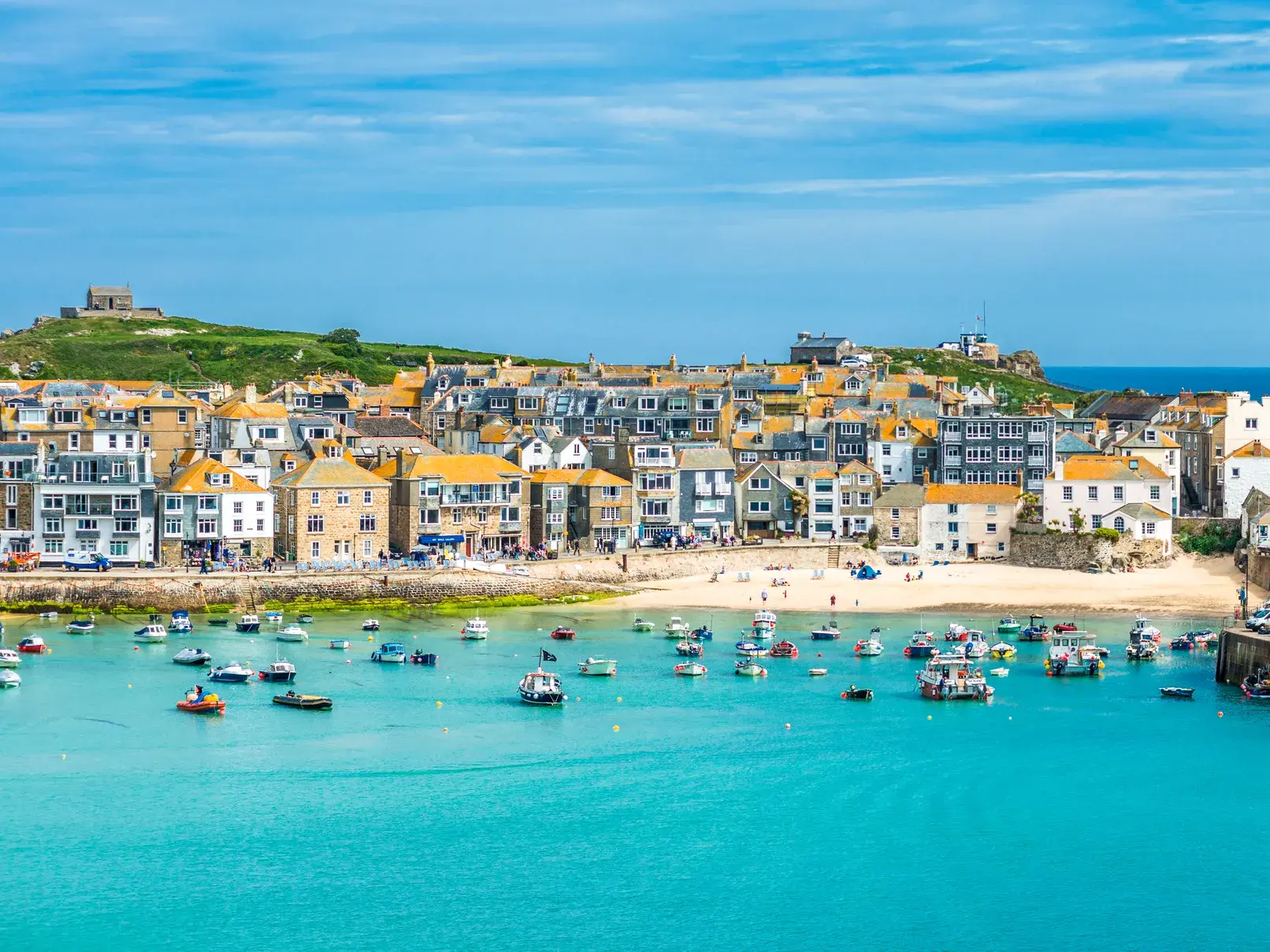 Malerischer Blick auf das Küstenstädtchen St Ives in Cornwall mit Sandstrand und vielen Booten in der türkisblauen Bucht.