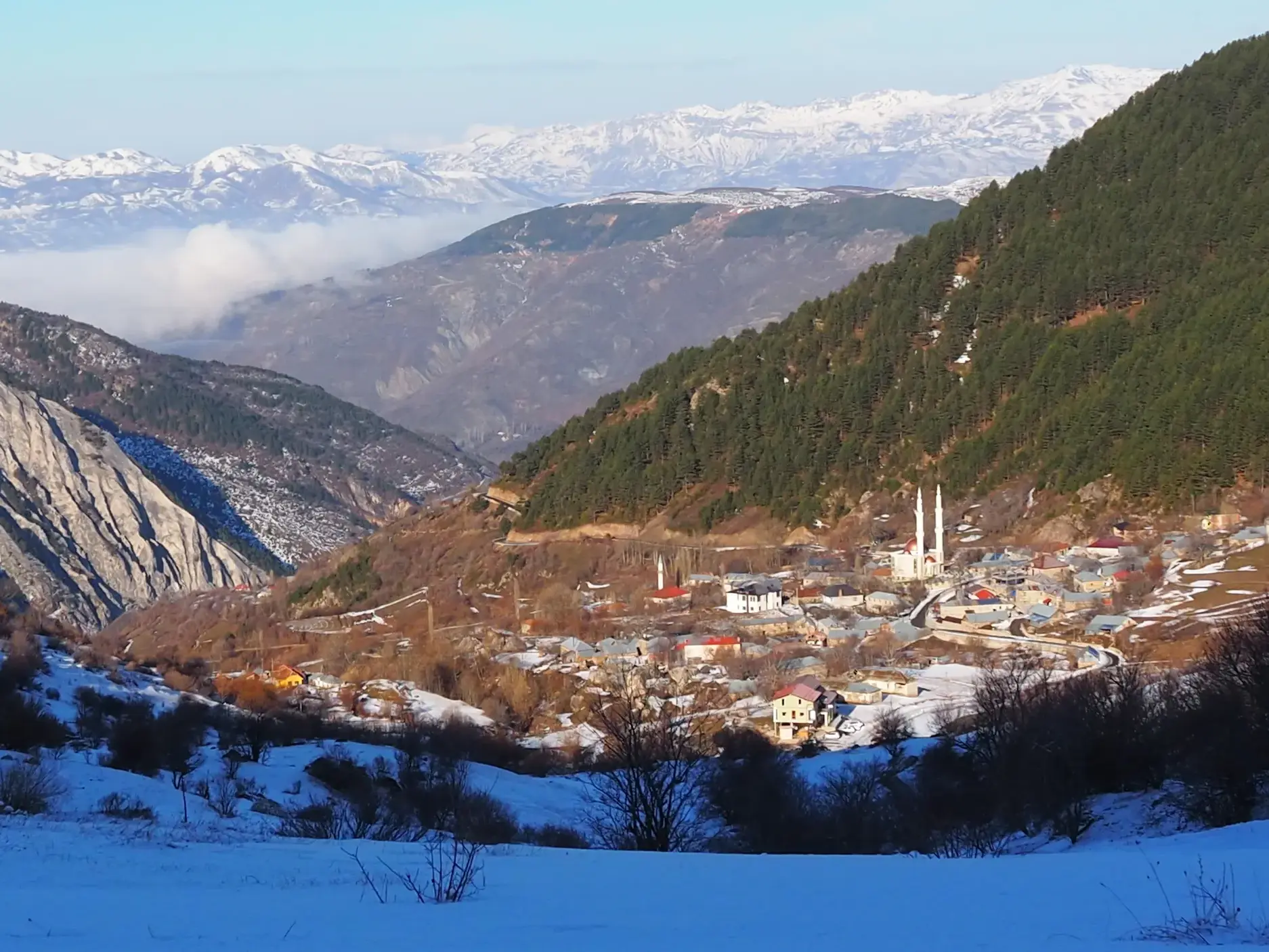 Blick von einer Skitour auf das verschneite Dorf Radomire in Albanien, im Hintergrund die Gipfel des Korab-Koritnik Gebirges.