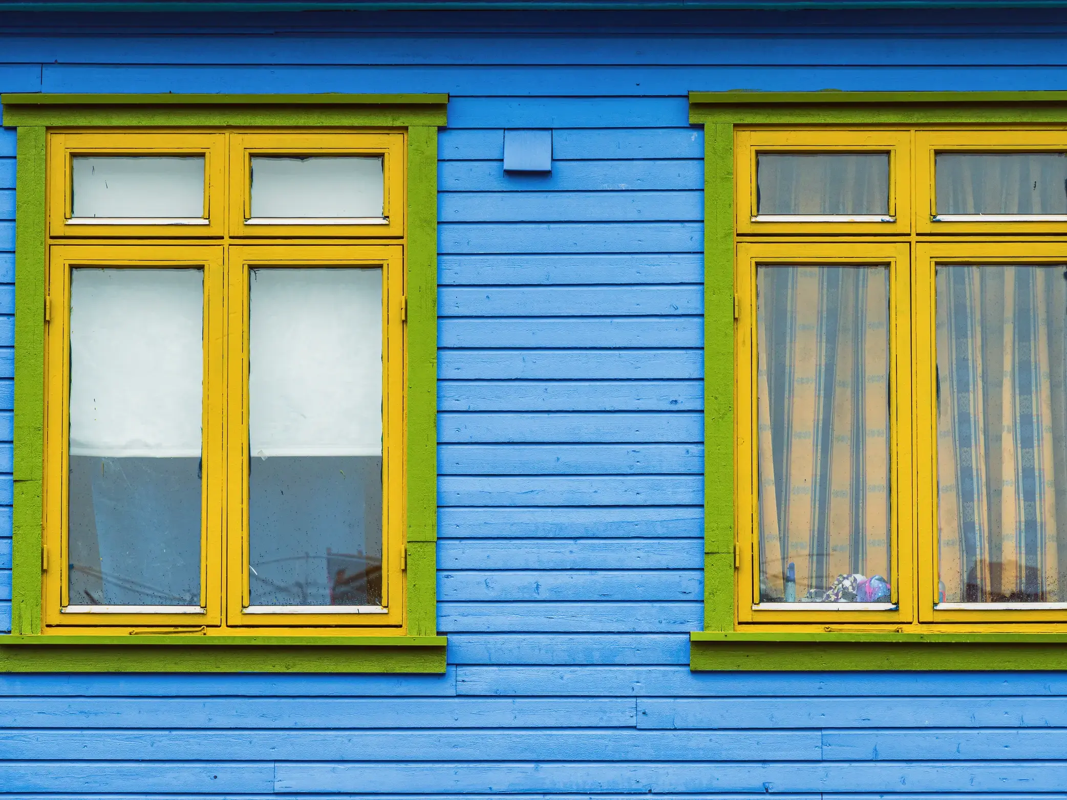 Detailansicht der farbenfrohen Holzfassade eines Hauses im Hanseviertel Bryggen in Bergen mit gelben Fenstern.