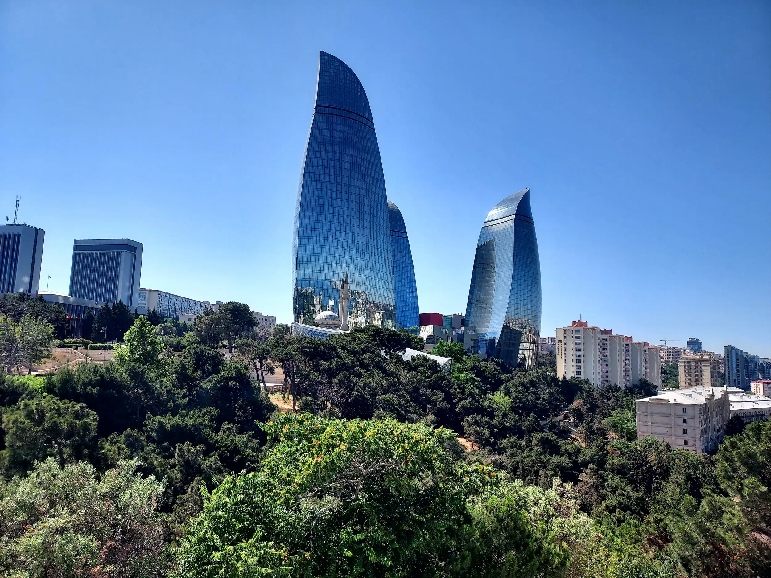 Die futuristischen Flame Towers ragen über eine grüne Parklandschaft in den blauen Himmel über der Skyline von Baku, Aserbaidschan.