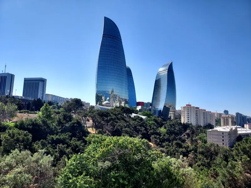 Die futuristischen Flame Towers ragen über eine grüne Parklandschaft in den blauen Himmel über der Skyline von Baku, Aserbaidschan.