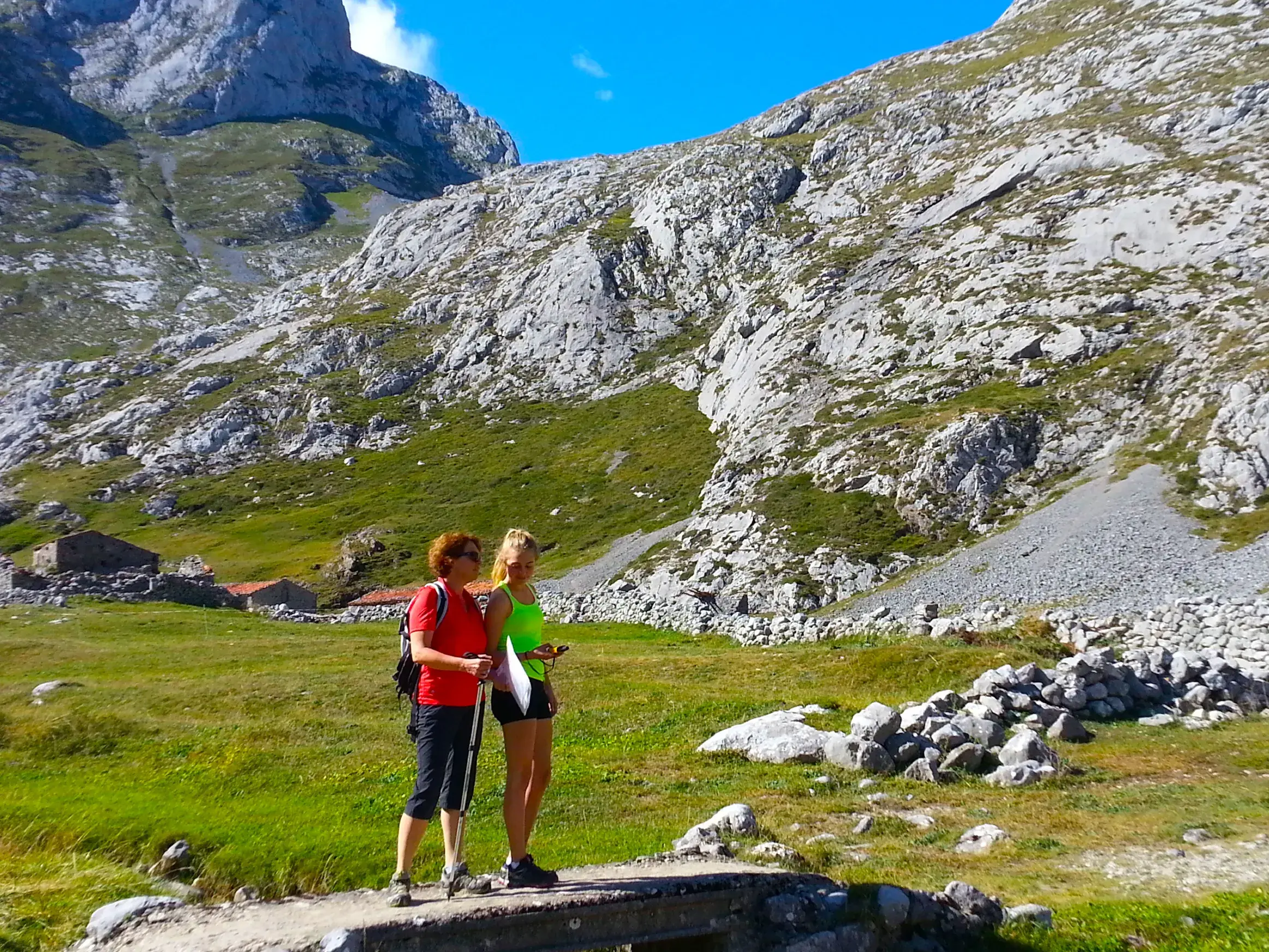 Zwei Wanderinnen orientieren sich mit einem Roadbook auf einer Brücke vor der kargen Felslandschaft des Ándara-Massivs.