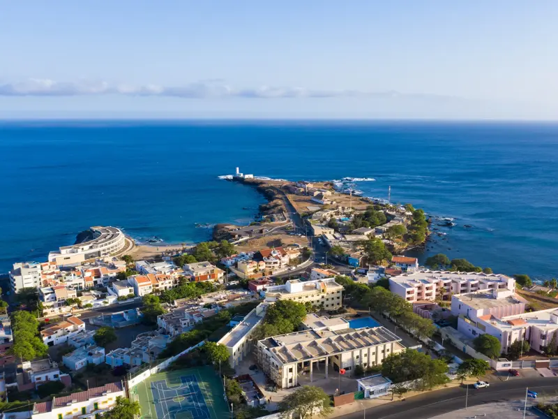 Luftaufnahme der Küstenstadt Praia auf Santiago, Kapverden, mit einer in den blauen Atlantik ragenden Halbinsel mit Leuchtturm.