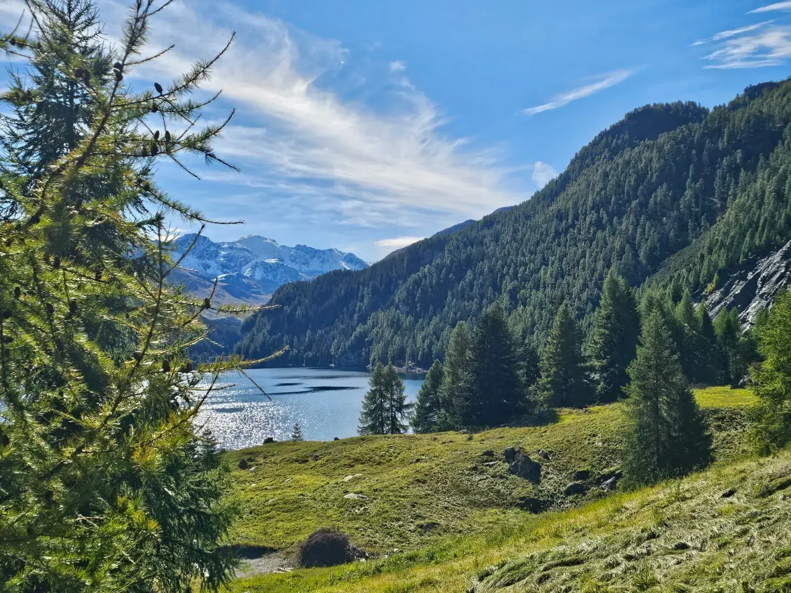 Beim Wandern in Graubünden eröffnet sich der Blick auf einen blauen Bergsee vor schneebedeckten Alpengipfeln.
