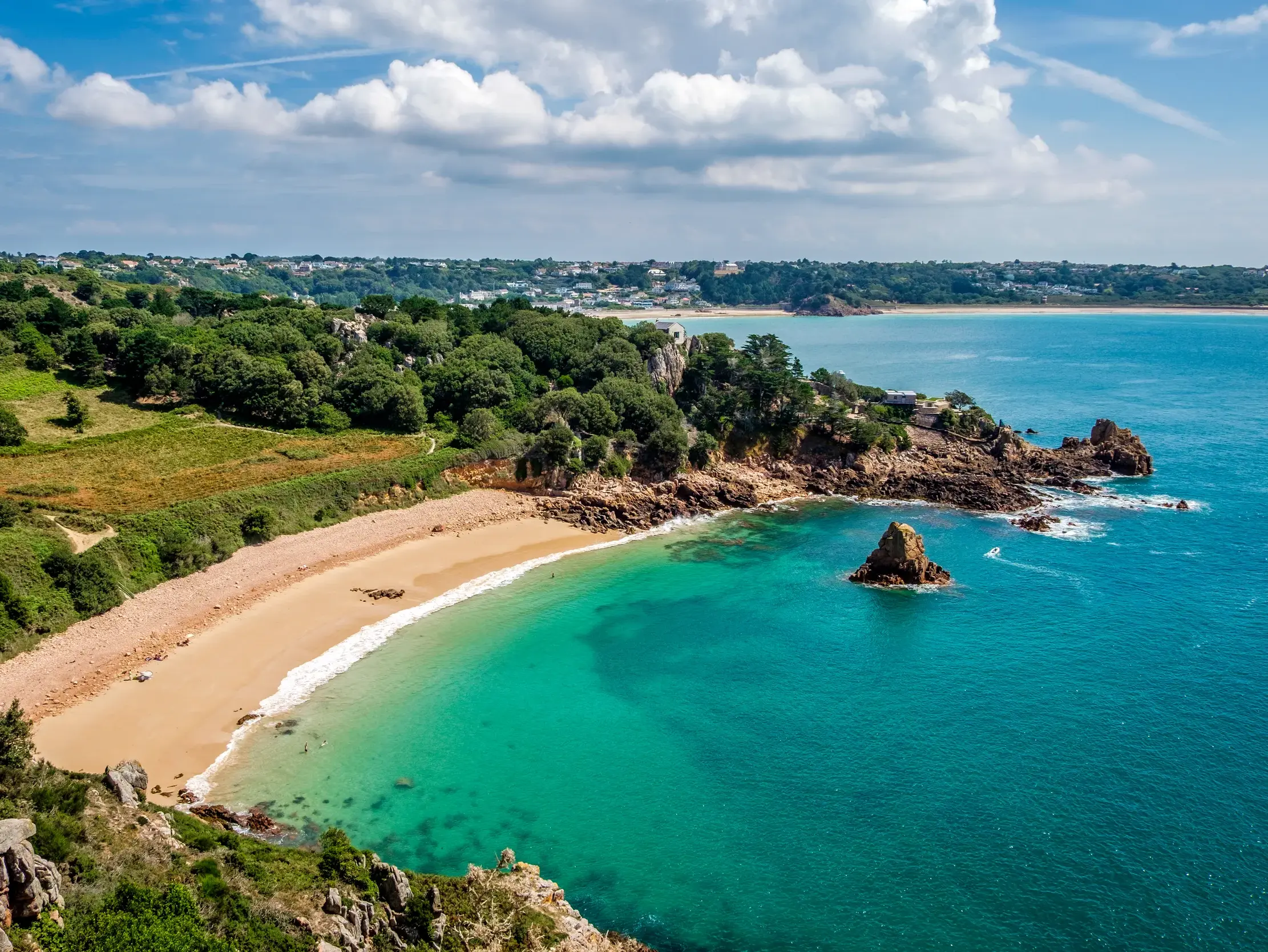 Malerische Bucht auf der Kanalinsel Jersey mit goldfarbenem Sandstrand, türkisfarbenem Wasser und üppig grüner Küste.