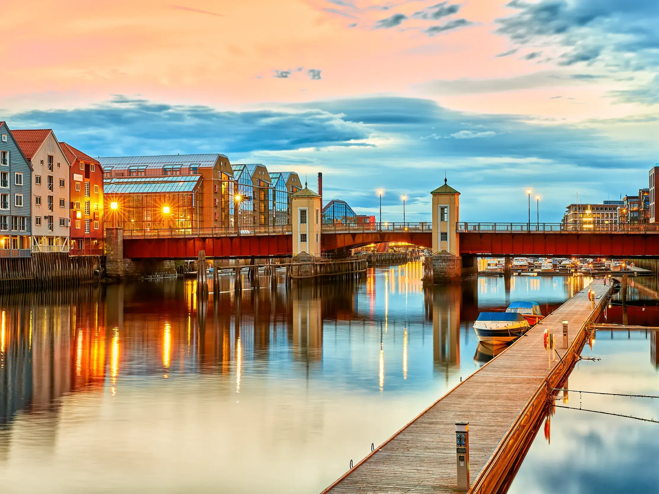 Bunte Speicherhäuser und die alte Stadtbrücke Gamle Bybro in Trondheim spiegeln sich im Nidelva-Fluss bei Sonnenuntergang.