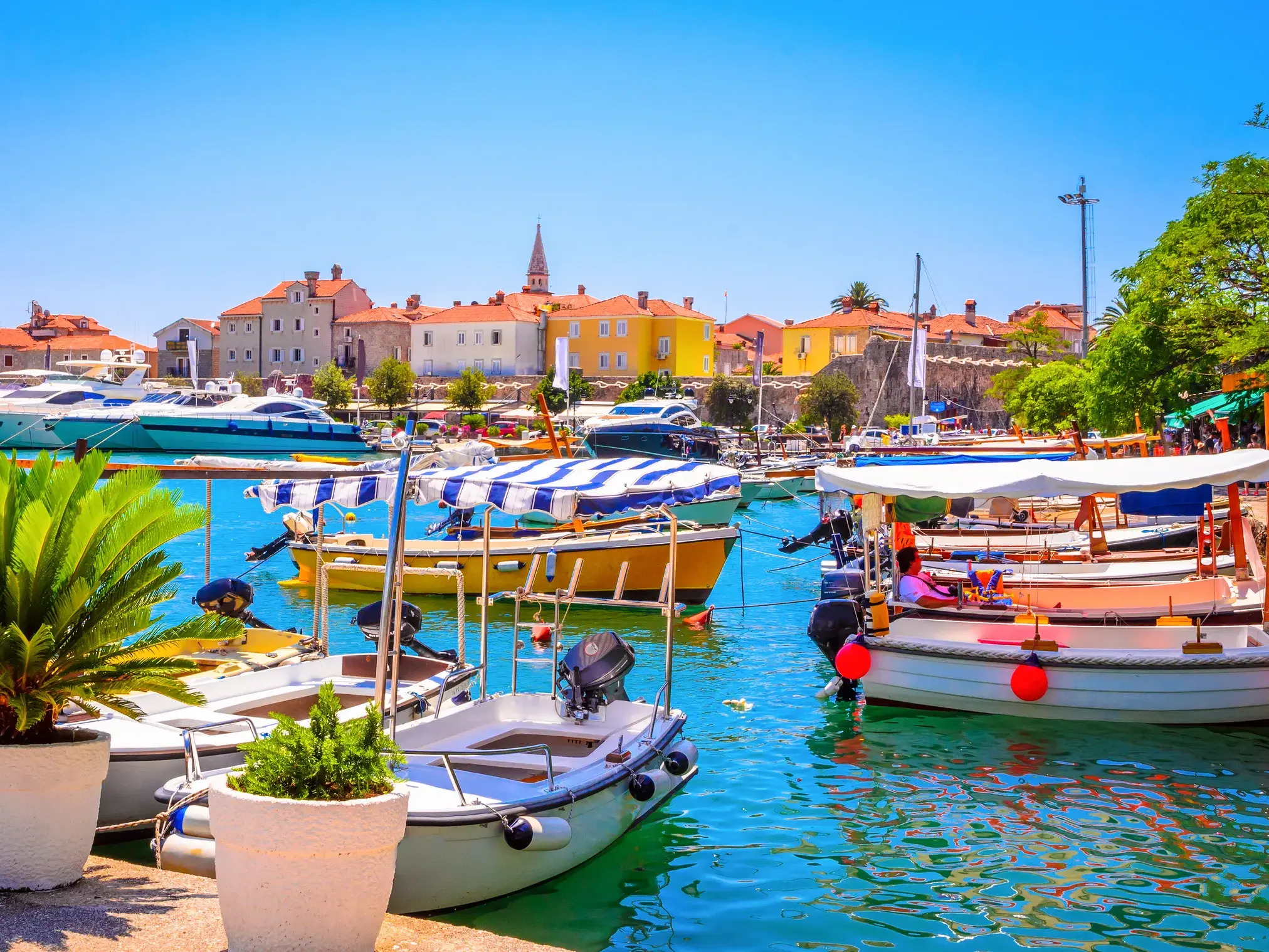 Kleine Boote und Yachten ankern im sonnigen Hafen von Budva mit Blick auf die historische Altstadt an der Adria.