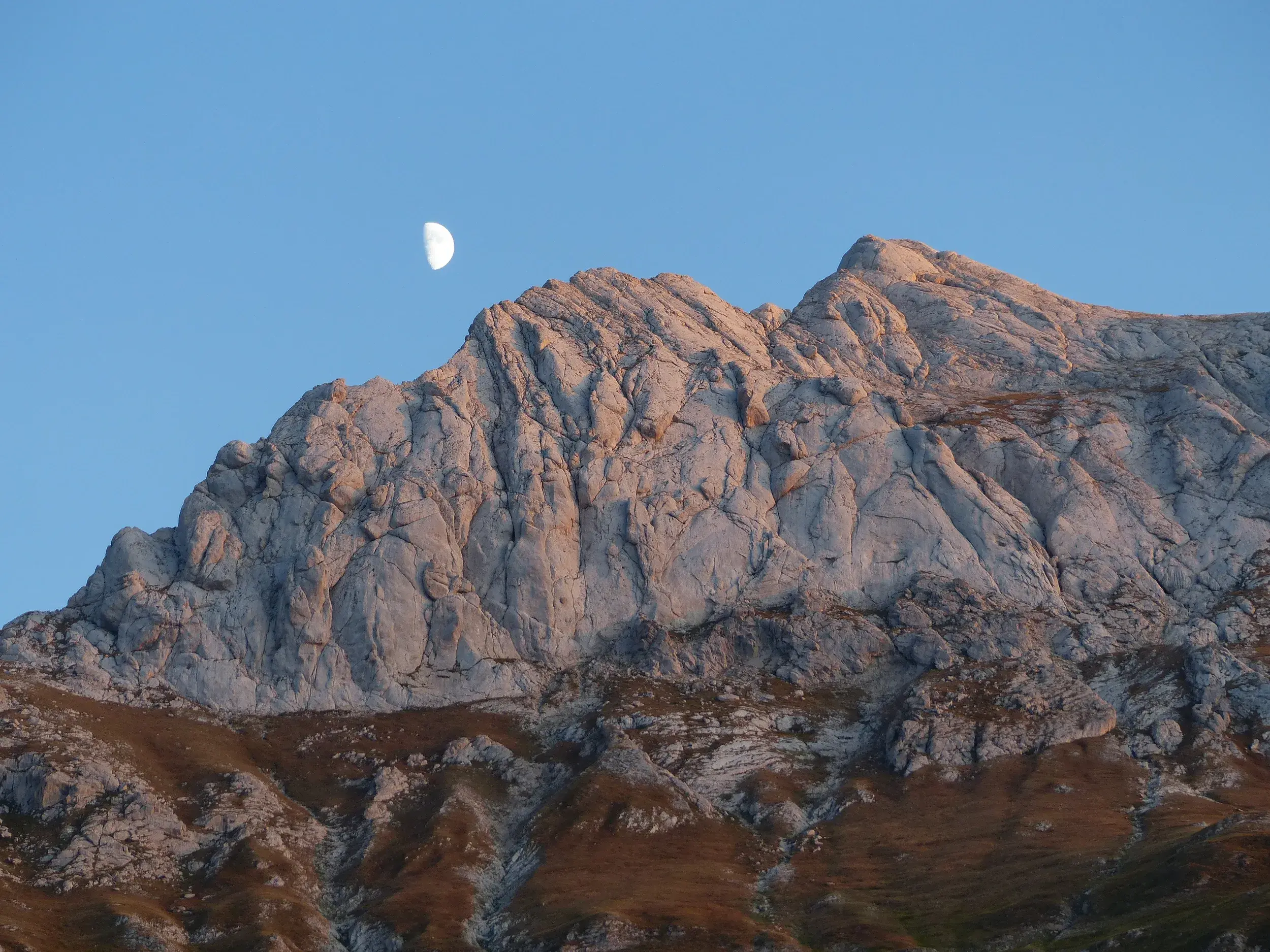 Ein Halbmond scheint am blauen Himmel über einem zerklüfteten Felsgipfel im Nationalpark Gran Sasso in den Abruzzen.