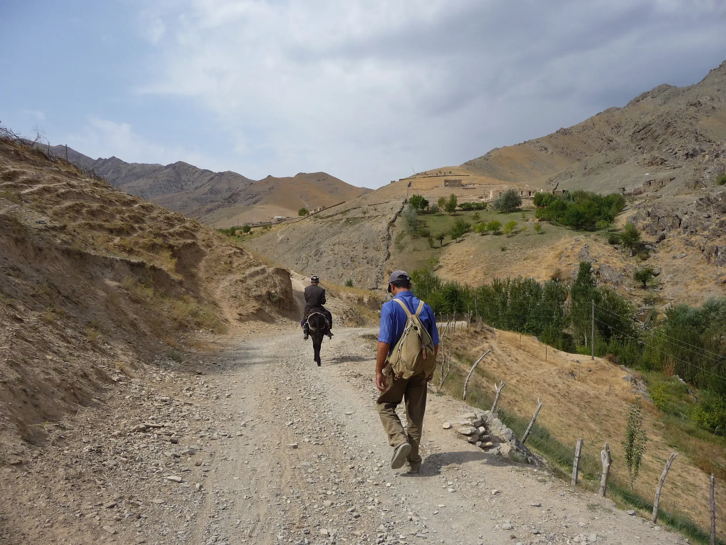 Ein Wanderer folgt einem Einheimischen auf einem Esel auf einem Schotterweg durch das karge Nuratau-Gebirge in Usbekistan.