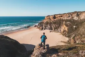 Wanderer auf einer Klippe an der Rota Vicentina blickt auf eine einsame Sandbucht und den Atlantik an der Algarve.