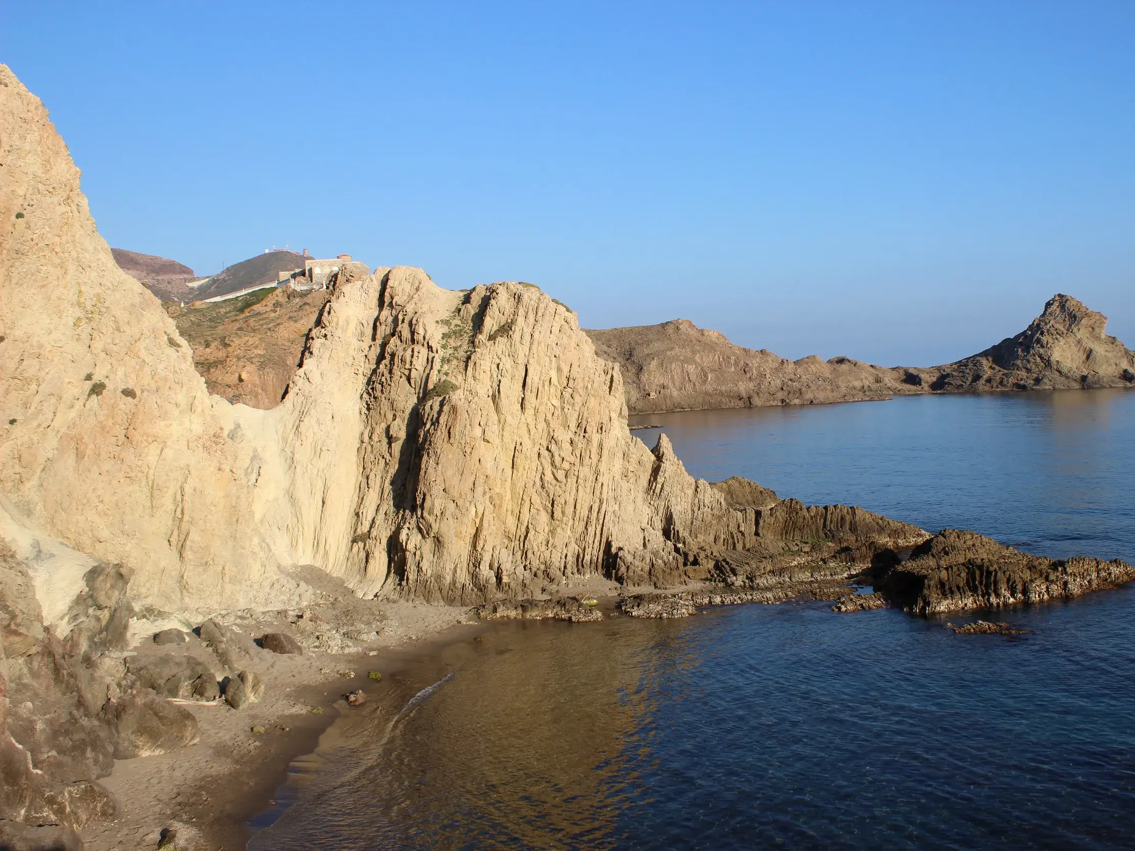 Schroffe, sonnenbeschienene Felsklippen und eine kleine Bucht an der Küste des Naturparks Cabo de Gata in Andalusien.